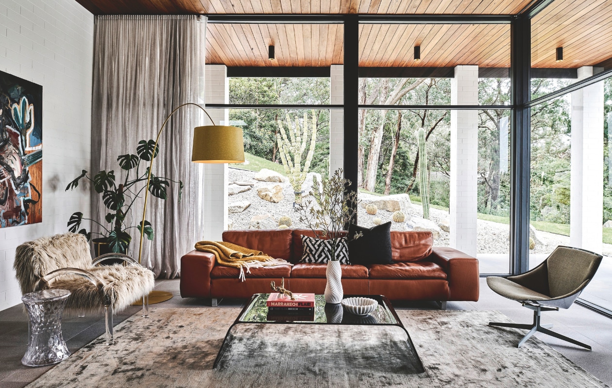 Vloerlamp Twiggy van Marc Sadler voor Foscarini. Fauteuil Wylie van En Gold. Schilderij van Toby William Taylor Raine. De leren bank is laag, waardoor hij het zicht op de tuin niet wegneemt. Fauteuil rechts Space Lounge van Jehs Laub voor Fritz Hansen. Op de salontafel staan accessoires van Frey. Stijlvol wonen 05-2025 | fotografie Tom Blachford | tekstbewerking Evelien Roels