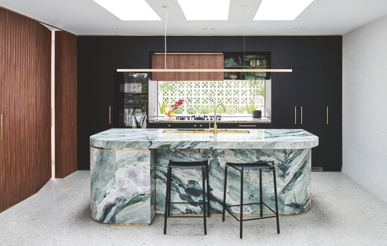Hanglamp Giffin Design. Het Calacatta Verde-marmer voor het eiland kreeg ronde hoeken in de looproute, en messing details die de belijning versterken. Kasten maatwerk.  Deurbeslag Designer Doorware. Wandbekleding Screenwood. Krukken StyleCraft. Op de vloer ligt terrazzo. Dakramen Velux. Stijlvol wonen 05-2025 | fotografie Tom Blachford | tekstbewerking Evelien Roels
