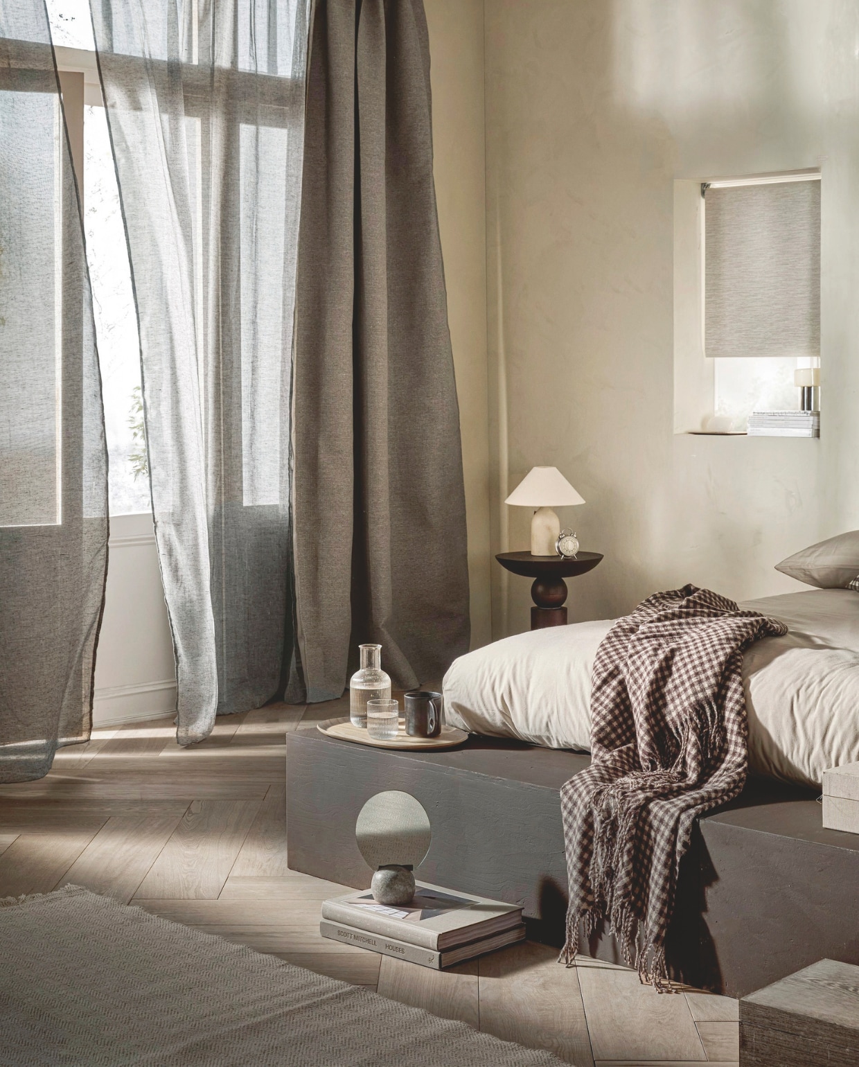 Verduisterend rolgordijn Sand, 60x190 cm (bxh) € 83,99, verduisterend gordijn Drizzle in Mirre, met plooi,  140x270 cm (bxh) € 73,99 en halftransparant gordijn Frost in Grijs, met plooi, 140x270cm (bxh) € 50,99.M.m.v. vestingh.nl (kalkverf Chalk van Lab in Just Jimmy), zarahome.com (tafellamp, bijzettafel, wekker, karaf met glas, plaid, kleine tafellamp kozijn, ronde albasten tafellamp, dienblad), hm.com (mok, spiegel op voet, dekbedovertrek). Overig privébezit. vtwonen 06-2025 | styling Sanne Ketelaar | fotografie Peggy Janssen
