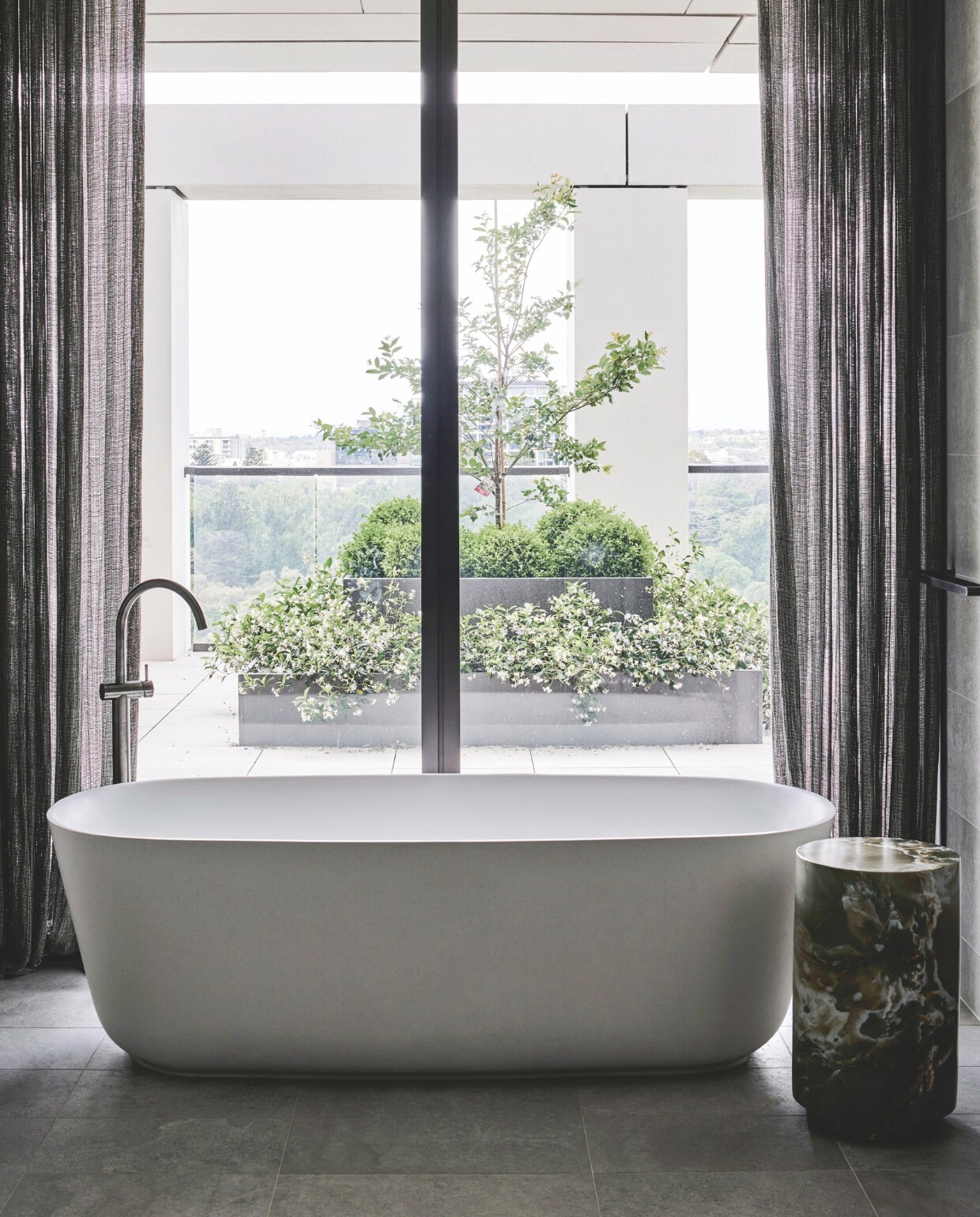 In de en-suitebadkamer is het bad zo gepositioneerd dat optimaal van het uitzicht genoten kan worden. Bijzettafel Herbie van Arteriors via Boyd Blue. Stijlvol Wonen 05-2025 | styling Simone Haag | fotografie Tom Blachford
