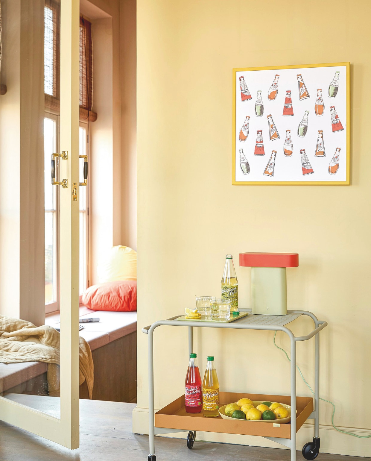 Stalen trolley Push van Hübsch in Sand/Brown € 290,-, glazen Sui van Hübsch € 6,-, tafellamp Sleek van Hübsch, staal en polycarbonaat € 160,- (shop.vtwonen.nl). Poster Aperitivo door Enik Eged, gele houten lijst € 58,- (pstrstudio.com). Biologisch percal-katoenen kussensloop Big Dot in Yellow € 44,95, in Orange € 59,95 (suite702.com). Plaid Quilted, linnen, katoen en polyester € 109,- (hkliving.com). Overig privébezit. vtwonen 06-2025 Styling Hello Yellow | styling Kelly van Gendt | fotografie Peggy Janssen