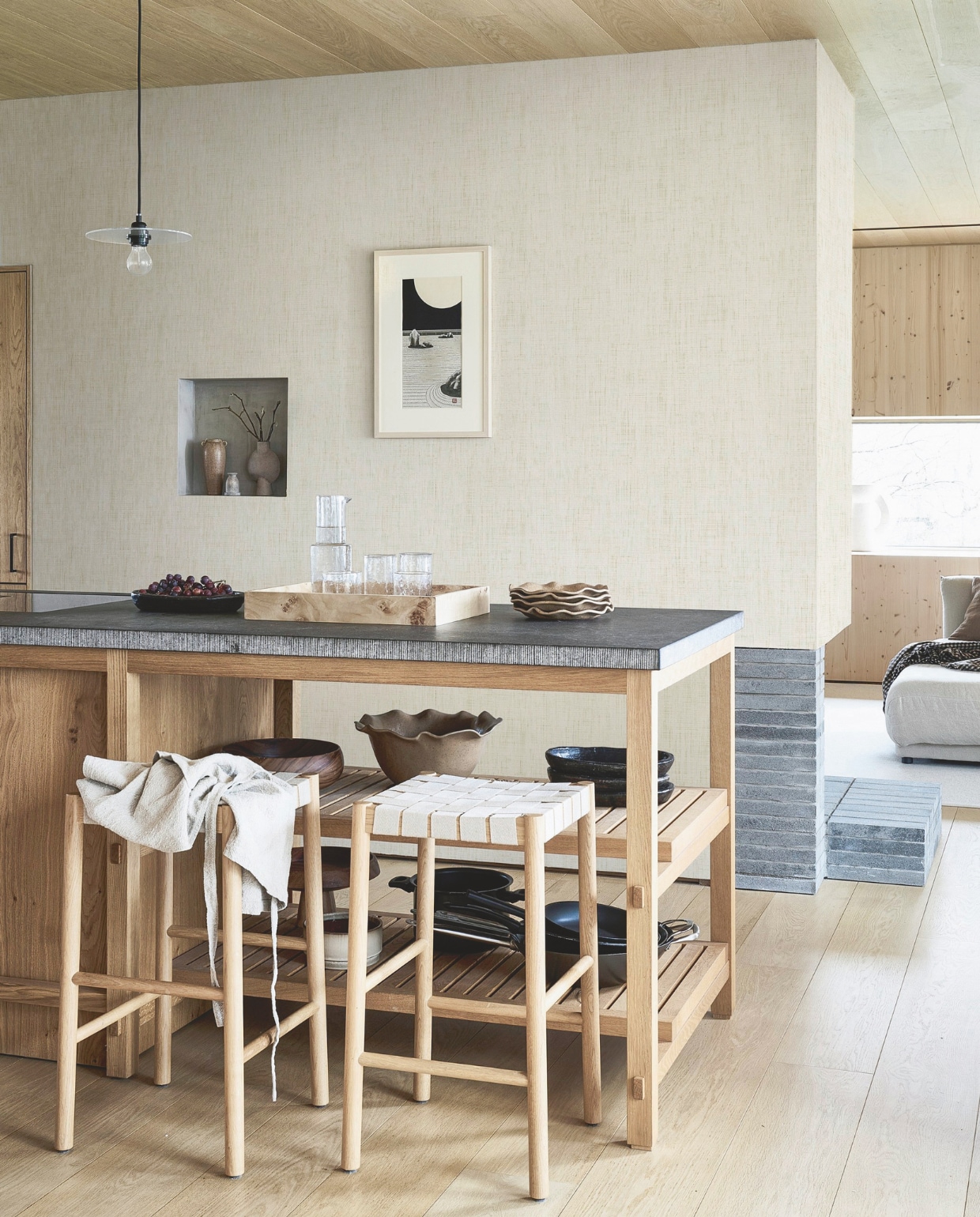 Behang Linnen in Gold, 53 cm x 10 m (bxl), per rol € 33,99.M.m.v. zarahome.com (houten dienblad, karaf en glazen, bruine vaas, schaal en borden met geschulpte rand, zwarte borden), andtradition.com (barkrukken), 101cph.com (taupe vaas Sphere Bubl Mini), timelesslinen.com (schort), framacph.com (hanglamp Circle Shade). vtwonen 06-2025 | styling Kim van Rossenberg | fotografie Sjoerd Eickmans