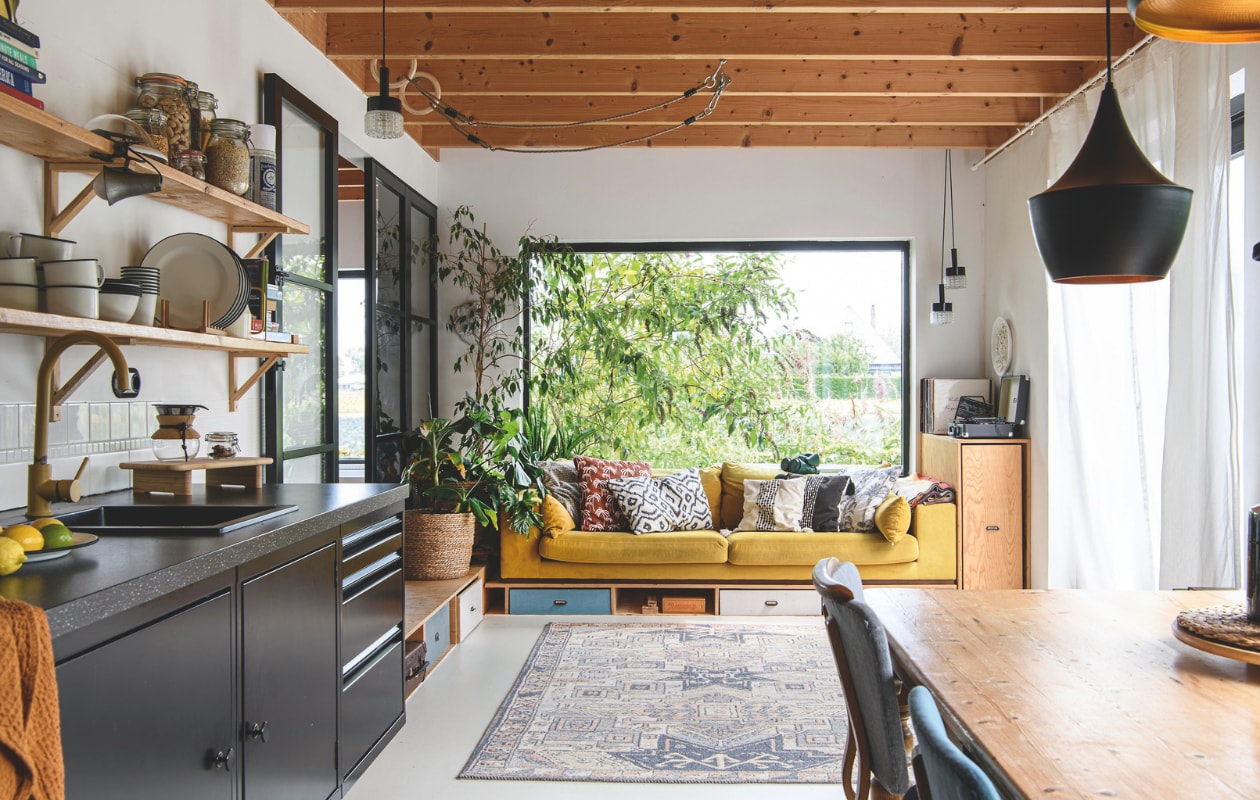 Plantenmand en koffer kringloop. Gietvloer Stamvloeren. Houten kasten zelfgemaakt, hanglampen Marktplaats. Vloerkleed en bank Nous Living. Kussens Wehkamp, H&M Home en Zara Home. vtwonen 06-2025 | styling Fiona Richardson | fotografie Lisa Cohen