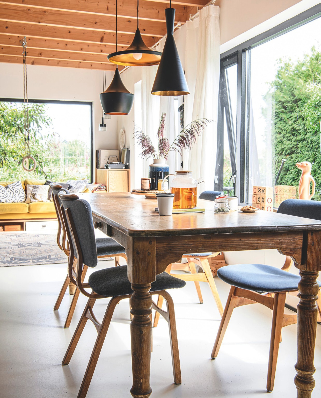 Tafel Marktplaats, eetkamerstoelen zelf opnieuw bekleed en opgeknapt. Gietvloer Stamvloeren, lampen boven eettafel Beat van Tom Dixon. Vloerkleed en bank Nous Living, mok Dille & Kamille. Weckpot, vaas, plantenmand, theepot en vaas kringloop. Ringen De Bruine Schommel, houten boter-kaas-en-eierblokken Outdoor Play. Houten kasten, lades onder bank zelfgemaakt. Potje honing The Bee. Kussens Wehkamp, H&M Home en Zara Home. Oude platenspeler Maxiaxi, hanglampen Marktplaats, glazen lampjes Catawiki. vtwonen 06-2025 | styling Fiona Richardson | fotografie Lisa Cohen