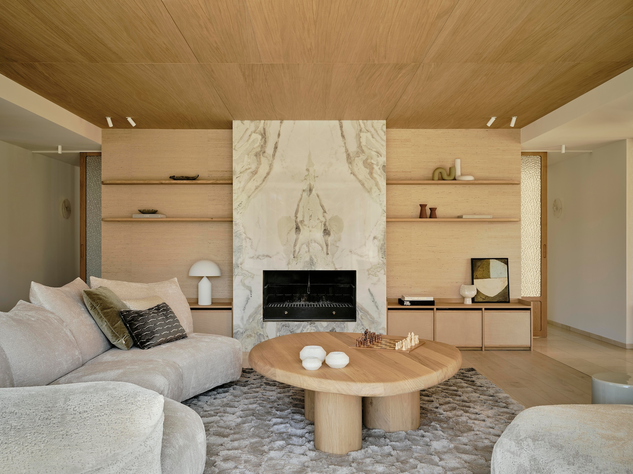 Modulaire bank Edra. Kussens gemaakt door Stoffeershop en bekleed met stof van Dedar en Zimmer + Rohde. Kleed Ferreira de Sá. Tafel Behout. Vazen Serax. Items planken links Maravillas, items planken rechts Roomer Art, Serax, HKliving. Tafellamp Oluce Atollo. Schouw Dover wit marmer. Zeegras behang Kudzu van Arte. stijlvol wonen 7-2025 | fotografie Space Content Studio