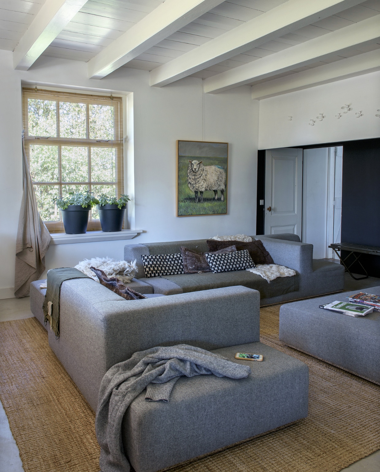 De woonkamer bevindt zich in de vroegere opkamer. De bank is van Sur + Plus, vloerkleed en zwart-wit kussen van Ikea, legerzak en plaid van Stapelgoed, plantenpotten van Karwei. De vilten kussens en kleden maakte Miranda zelf. Het schilderij is van Maja Philips. Op de wand witte bloemen van Umbra, als een knipoog naar ouderwetse wandbordjes. vtwonen 11-2019 | styling Monique van der Pauw | fotografie Ton Bouwer