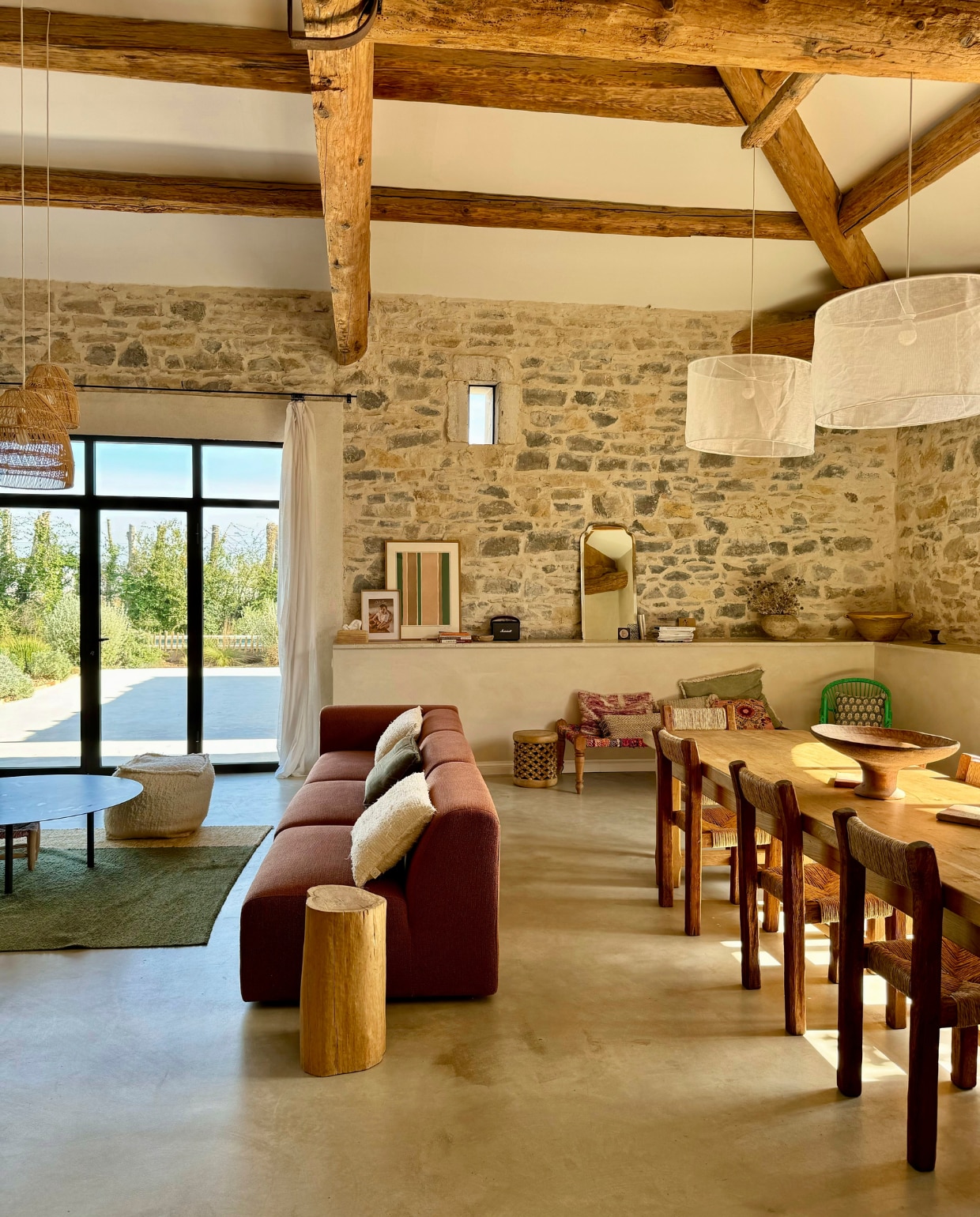 Hanglampen La Maison Pernoise. Stoelen in Brutalist-stijl geweven door Arnaud, tafel kringloop. Rotan hanglampen My Bohem. Vloer gepolijst beton, muren geschilderd met kalkverf van Mercadier in kleur Boumian. Banken By Sidde, metalen salontafels zelfgemaakt, katoenen kleed Saudade Design. Fauteuil Rua Madeira, rotan stoelen PK22 van Poul Kjaerholm voor Fritz Hansen. Travertin bijzettafel Talka. Groene installatie gemaakt van schijnhulst. vtwonen 07-2025 | fotografie Manon Ferra