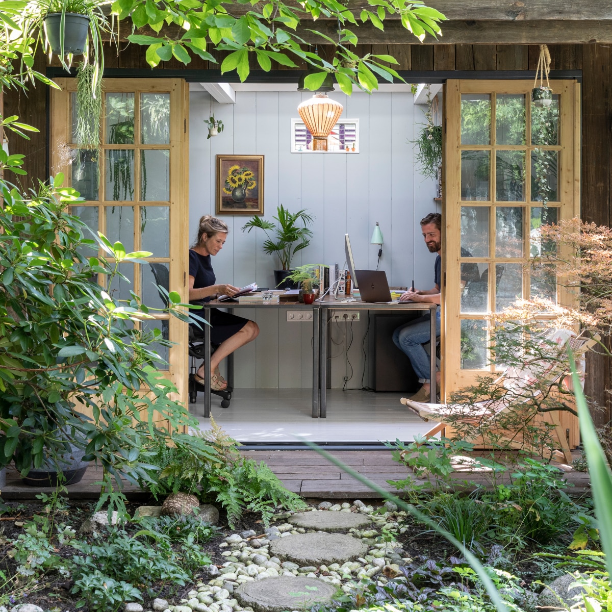 Tuinhuis ontworpen door Philip en gemaakt door timmermannen Jan en Rob. Deuren ’t Achterhuis. Planken op muur van oude schuren via Historisch Hout, net als de scheepsplanken op de veranda. Glas-in-loodraampje Marktplaats. Hanglamp Taiwan-lantern. Bureaus gemaakt door Mariekes vader. Schilderij aan muur uit Philips familie. Plantenhangers Mica. Wandlamp rommelmarkt IJ-Hallen. Strandstoel al jaren in bezit, herkomst onbekend. vtwonen 04-2020 | fotografie Margriet Hoekstra