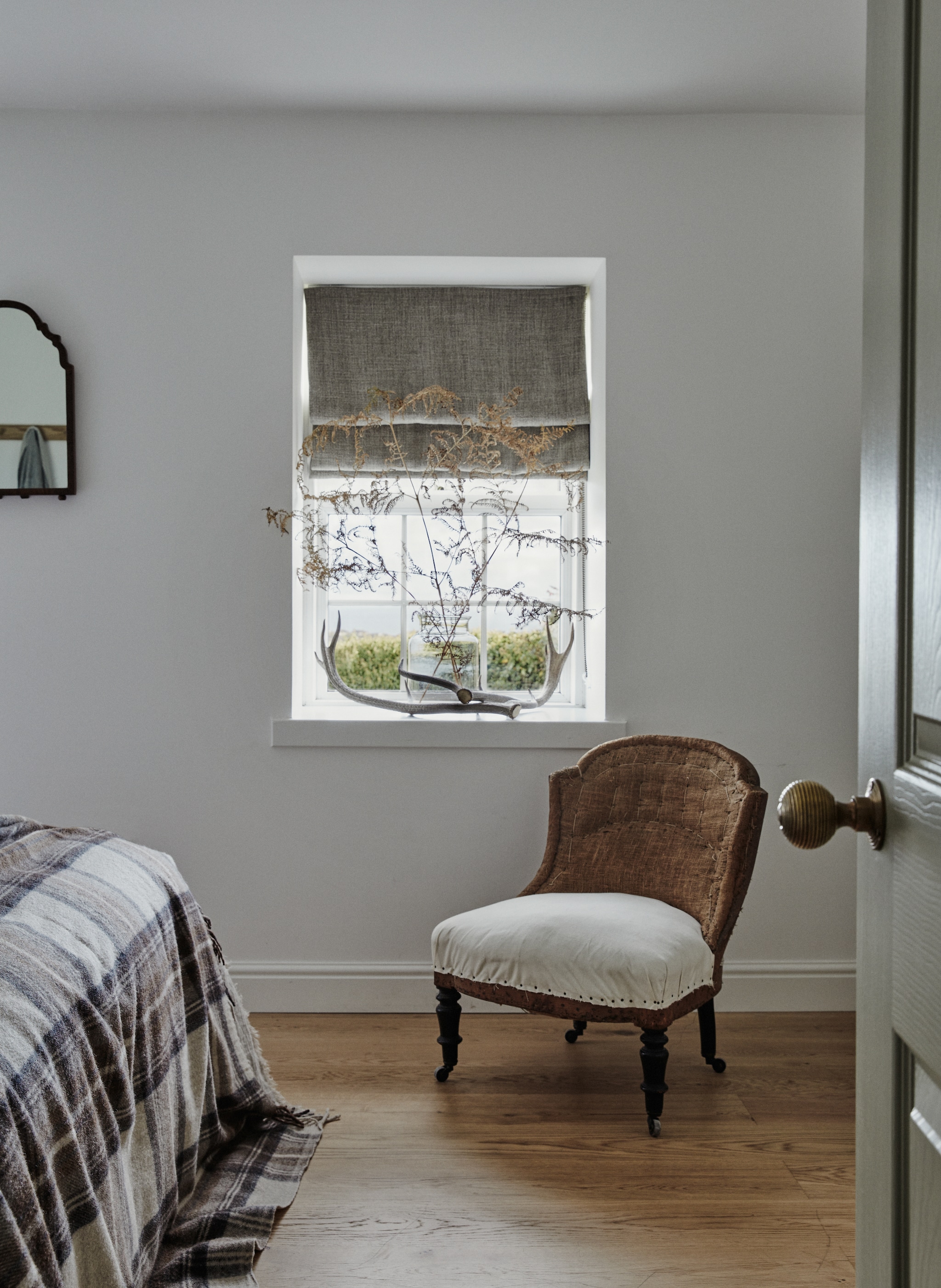 Op de muur van de tweede slaapkamer verfkleur All White van Farrow & Ball. Tartan plaid en bed van Feather & Black. Linen sprei Ellei Home. Lampen Original BTC. vtwonen Landelijk 9-2025 | productie Living Inside | styling Ali Heath | fotografie Brent Darby
