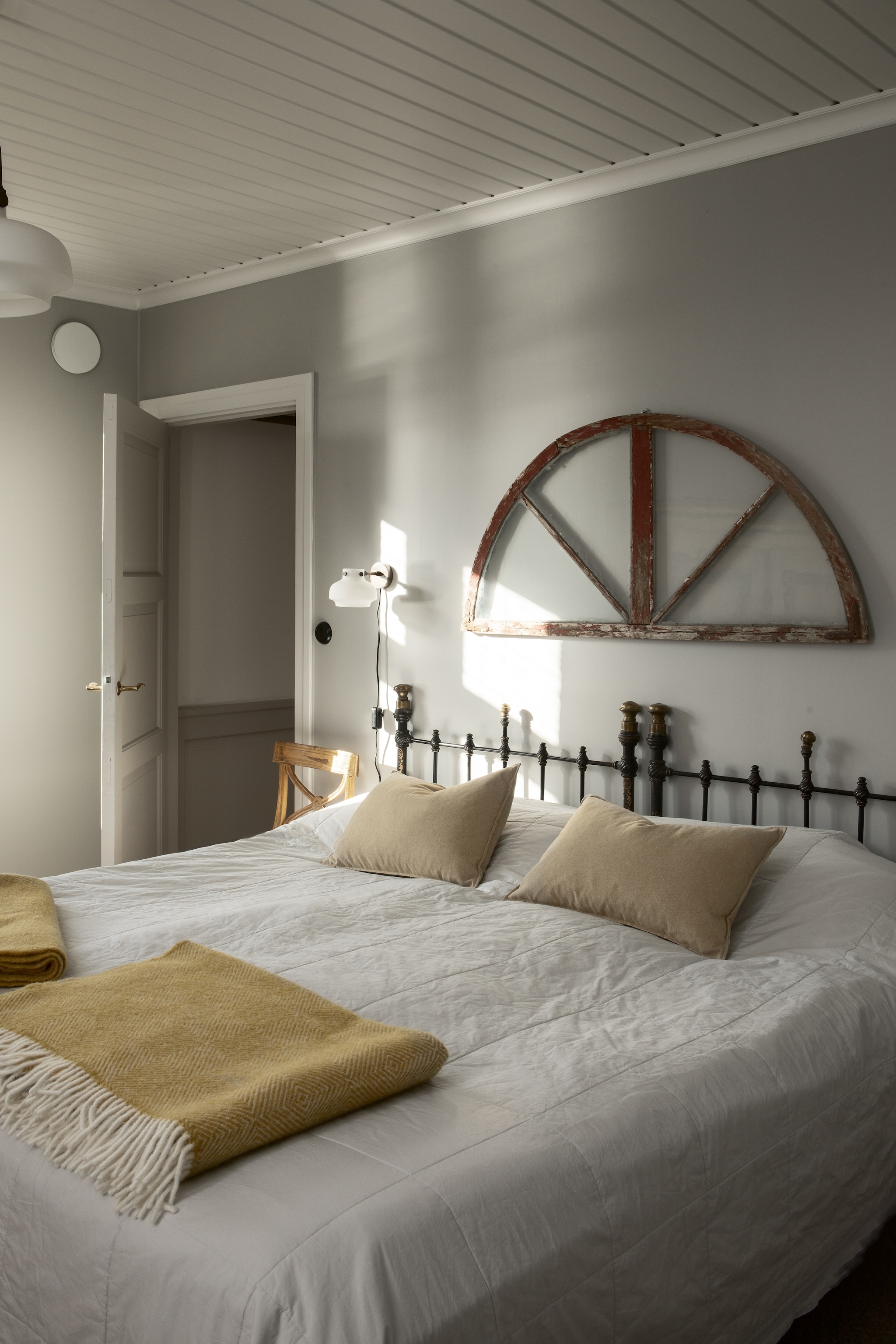 Hoofdbord onderdeel van het oude metalen bed van Charlotta’s oma. Lampen Copenhagen aan muur en plafond &Tradition. Houten stoel vintage. vtwonen Landelijk 9-2025 | productie Studio Rautio | fotografie Heikki Rautio