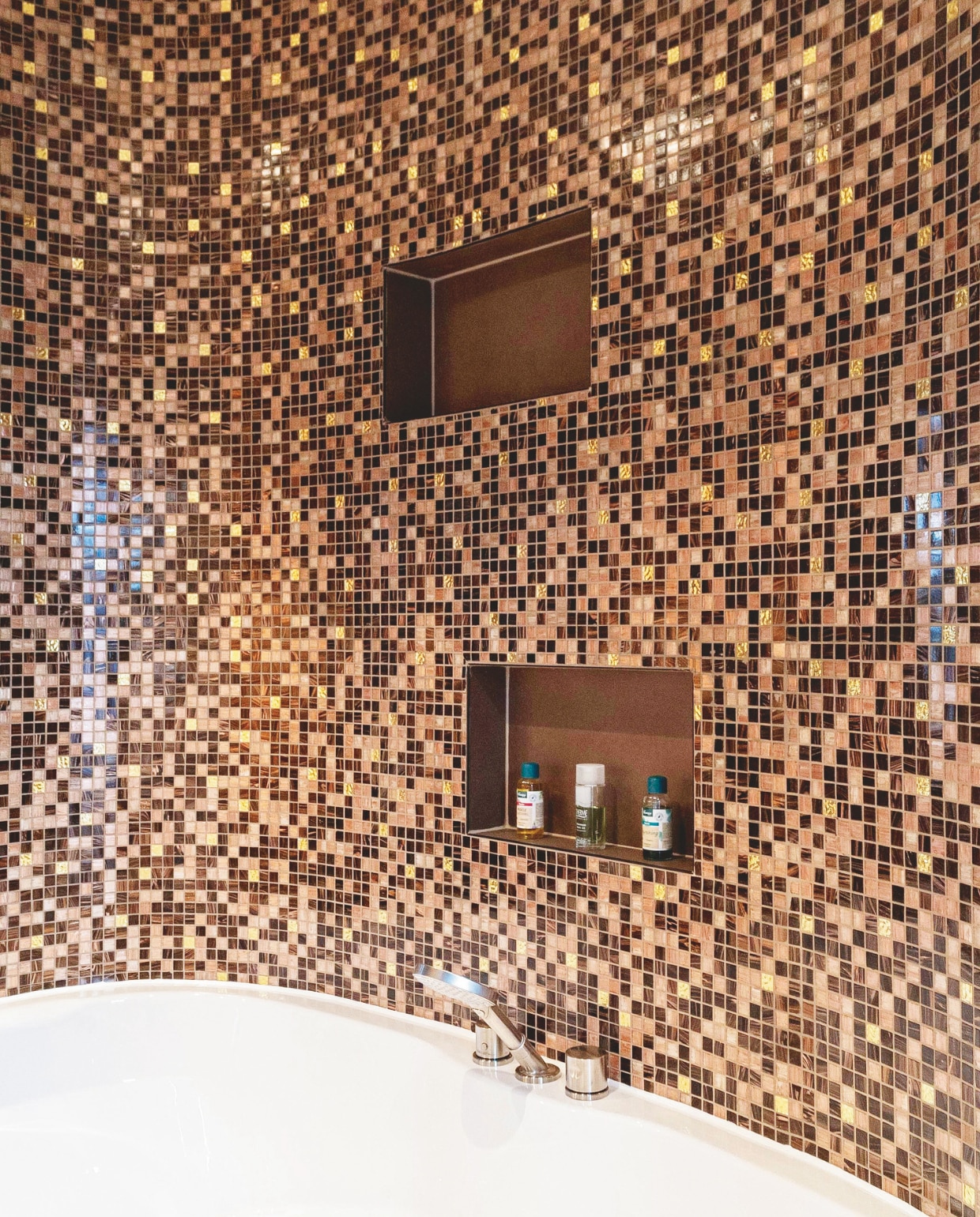 Ronde vormen en glinsterende muren vormen de ultieme combinatie voor een badkamer met allure. Diepeveen Keukens en Badkamers realiseerde dit unieke project. De wand bij het bad met whirlpoolsysteem is afgewerkt met mozaïektegels in warme koper- en bronstinten. Bij dat laatste sluiten de nissen voor verzorgings-producten perfect aan. diepeveen.nl Stijlvol wonen 05-2025 | dossier badkamers