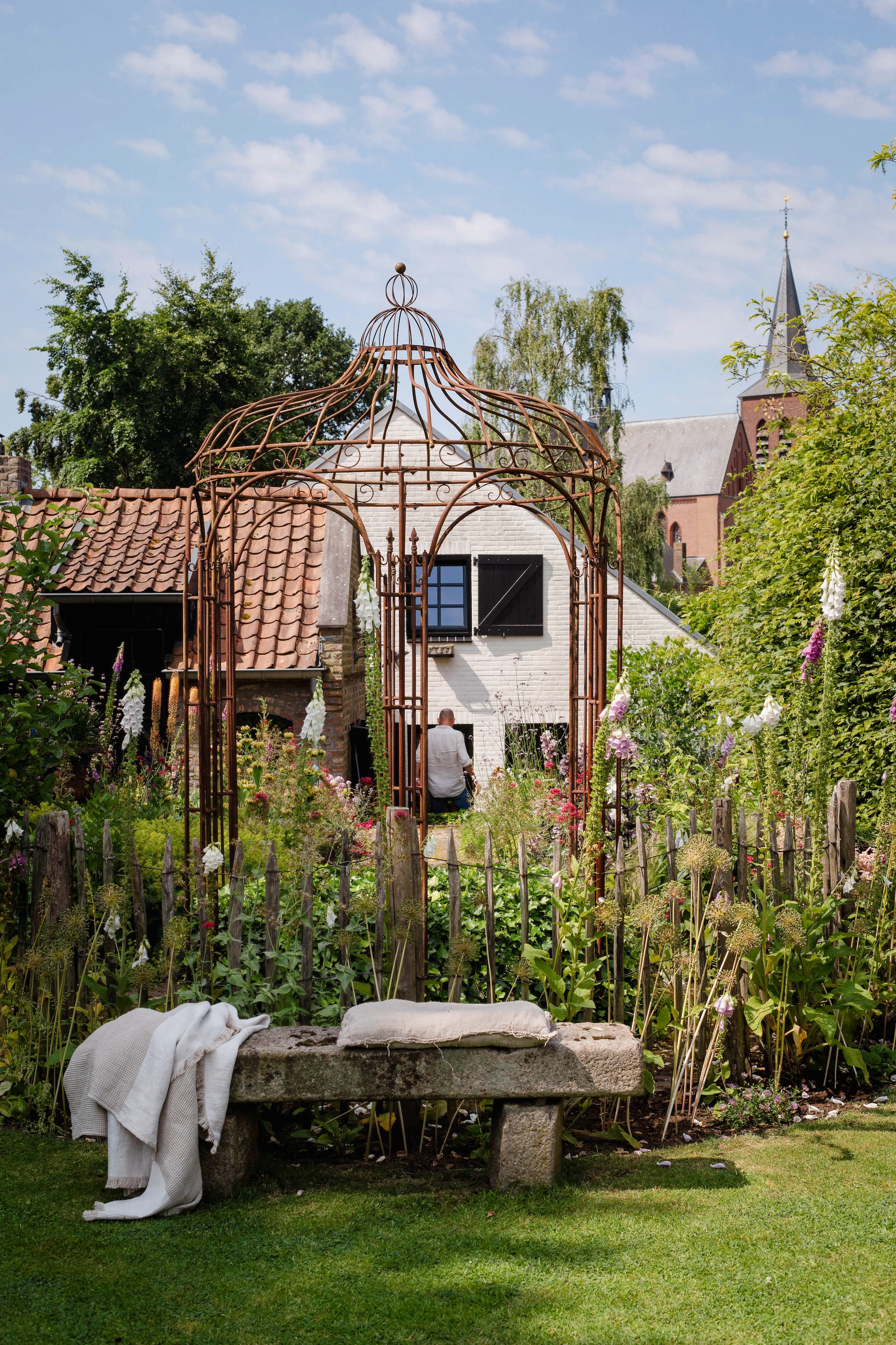 Doorkijkje vanaf het kerkpad dat naast de tuin en het huis loopt. De border is gevuld met ridderspoor, grassen, vingerhoedskruid en gaura.   vtwonen Landelijk 9-2025 | Fotografie Corine Hoge Bavel-Jansen