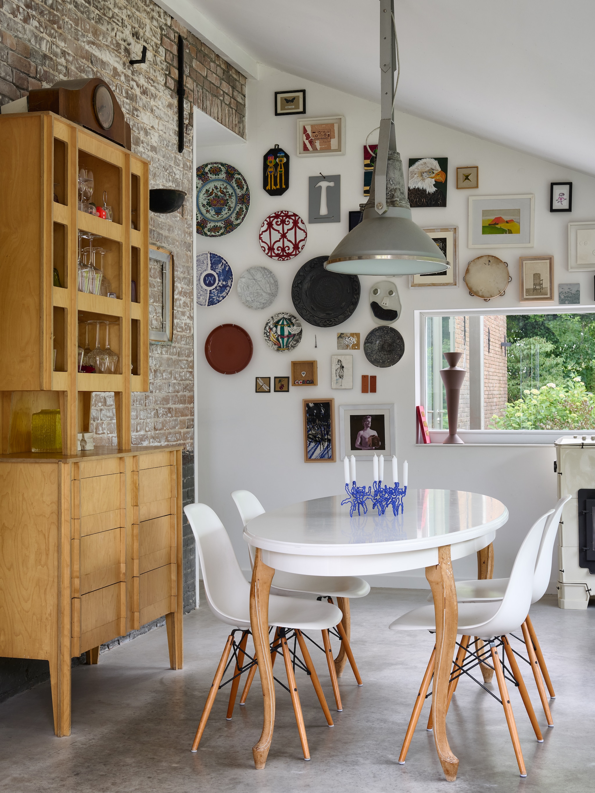 De kast is een prototype van de No Screw No Glue Cabinet van Joost. De poten van de samengestelde tafel komen van een tafel van Kiki’s grootmoeder. Eettafelstoelen Vitra Eames Dsw van Charles en Ray Eames. Aan de muur een bord van Hermès, verschillende objecten van Atelier NL, een bord van Fornasetti, keramiek werk van Maarten Baas, een foto van Sabine Pigalle en een originele tamboerijn van Eddie Vedder, de zanger van Pearl Jam. Op tafel staat een kandelaar uit het afstudeerwerk van Nick van Nechel. Uiterst rechts de houtkachel van Dick van Hoff voor Weltevree. Stijlvol Wonen 8-2025 | fotografie Kasia Gatkowska