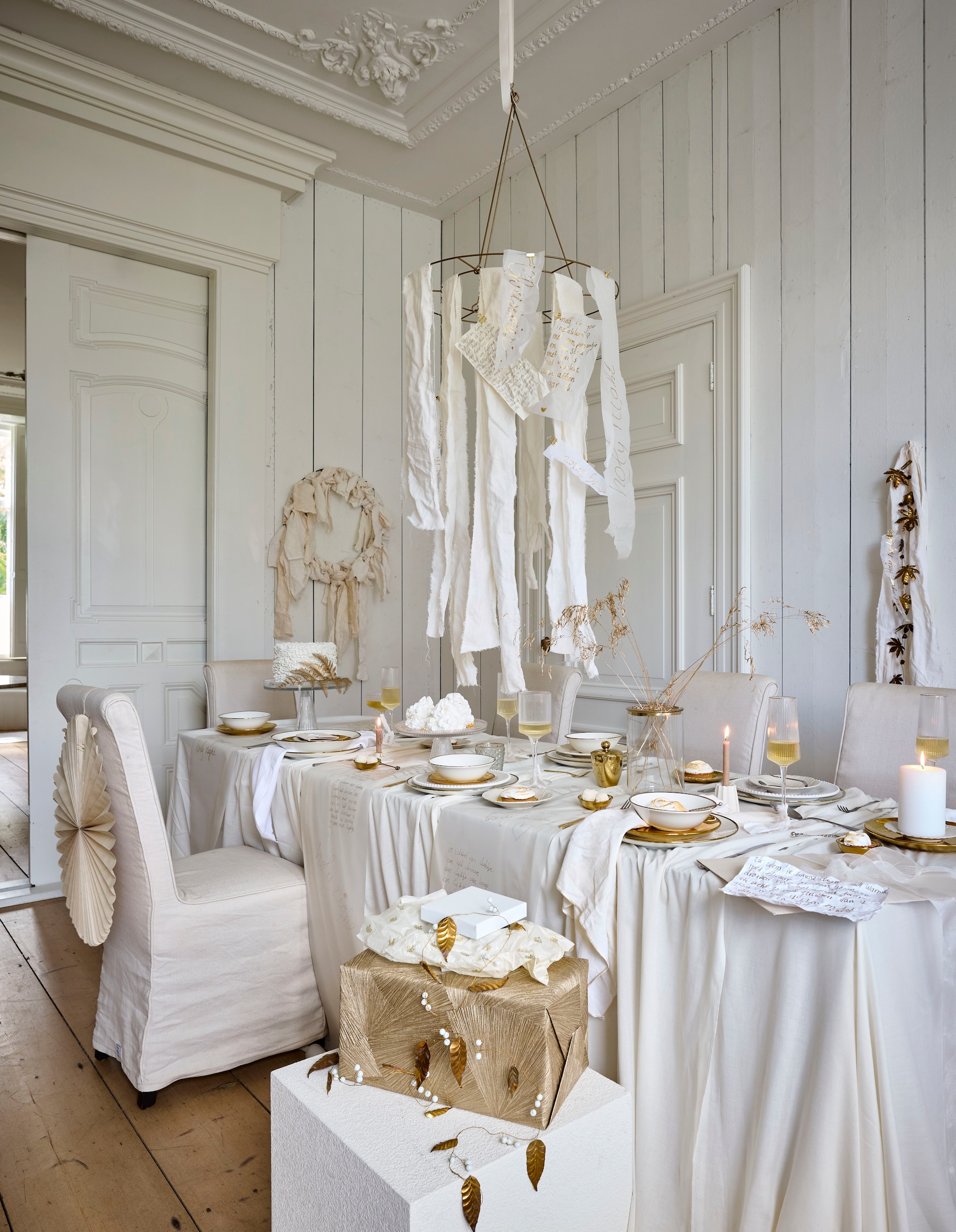 Zara Home bijzettafel, wit, 40x40x45 cm (lxbxh) € 199,- (zarahome.com). Vintage stoelen Rivièra Maison (marktplaats.nl). vtwonen decoratiering, metaal, goudkleurig, 60x61 cm (Øxh) € 29,95, kommen, porselein, wit/goud, set van 4 € 39,-, pastabord, porselein, wit-goud, set van 2 € 25,-, serviesset, porselein, wit-goud, 16-delig€ 125,-, bord, porselein, goud, set van 4€ 24,95,-, ontbijtbord, porselein, goud, set van 2 € 26,95, vaas, glas en metaal € 34,95, champagneglas, coupe, glas met gouden rand, set van 4  € 35,-, wijnglas, geribbeld glas met gouden rand, set van 4 € 35,-, champagneglas, flûte, geribbeld glas met gouden rand, set van 4 € 35,-, taartplateau, geribbeld glas, medium € 39,95, kandelaars, keramiek, wit € 12,95, kandelaars, keramiek, wit € 14,95 (shop.vtwonen.nl). Ikea rol tekenpapier Måla € 3,19,- (ikea.nl). H&m Home bord met bloemafdruk, keramiek € 9,99 (hm.com). MrsBloom sterren, papier, beige, slinger messing blaadjes en witte kralen, alles prijs op aanvraag (mrsbloom.nl). Søstrene Grene stompkaars, wit € 1,68 (sostrenegrene.com). Overig privébezit. vtwonen kerstspecial 2025 | styling Sanne Ketelaar | fotografie Alexander van Berge