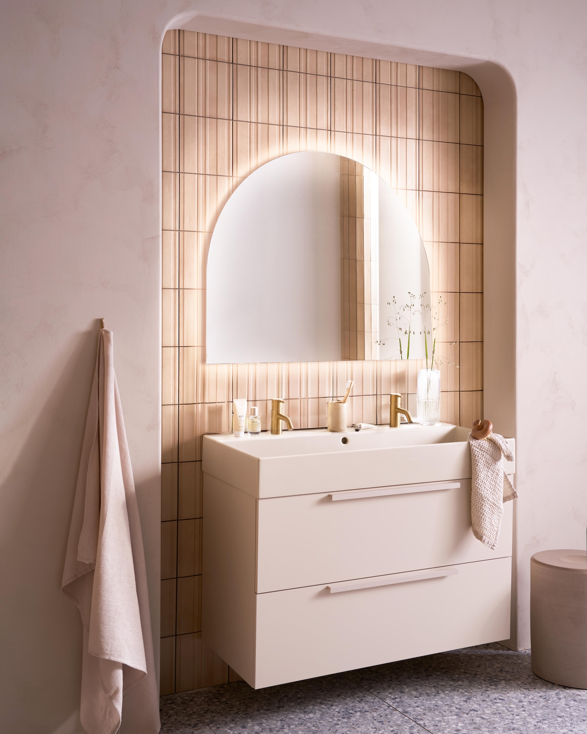 Op de wand tegels Earth Calce 3D Decor, 20x20 cm, per m² € 64,50. Op de vloer tegels Terrazzo Smoke Flakes, 60x120 cm, per m² € 74,50. Spiegel Design, half rond met indirecte verlichting, 100x80 cm € 998,-, ook verkrijgbaar zonder verlichting en in andere afmetingen. Kunststof onderkast Tidy in matzand, twee lades met handgreep, 120x40,5x40 cm (bxdxh) € 1362,-, Top Solid wastafel Wide in zand, twee kraangaten, 120x41x20 cm (bxdxh) € 1095,-. M.m.v. plieger.nl (kranen Roma in geborsteld goud), vtwonen.nl/shop (kruk van Serax), zarahome.com (badlaken, beker, zeep, kimono), lelabofragrances.com (parfum). Overig privébezit. vtwonen 09-2024 | fotografie Jeroen van der Spek | styling Cleo Scheulderman