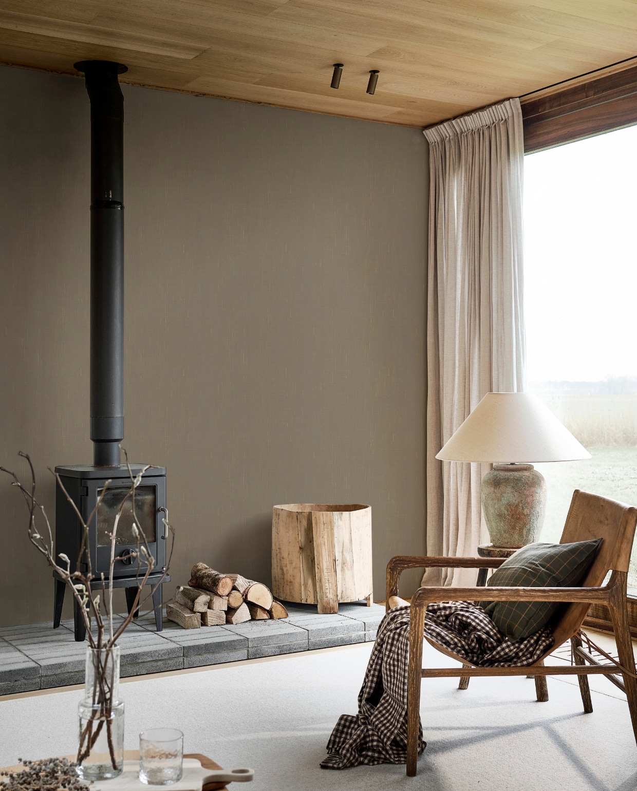 Behang Linnen in Mirre, 53 cm x 10 m (bxl), per rol € 33,99. M.m.v. hetkabinet.com (fauteuil, kruk, houten pot), zarahome.com (tafellamp, plaid, kussen, karaf, glas). Overig privébezit. vtwonen Landelijk 06-2025 | styling Kim van Rossenberg | fotografie Sjoerd Eickmans