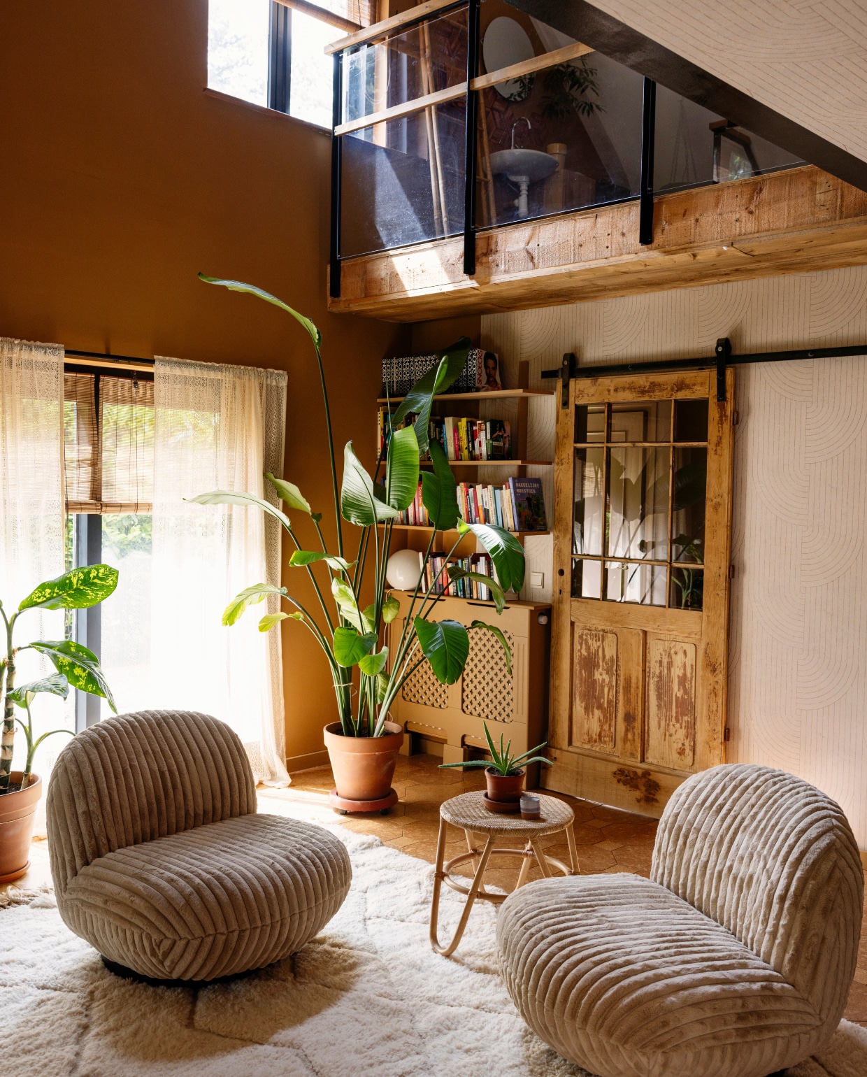 Muurverf in kleur Ig kh k-362 en vtwonen vliesbehang Broom bow flax (dessin 118159) van Karwei (ook tegenhet plafond). Draaifauteuils Swivel Fluffy Beige van Giga Meubel, vloerkleed Beni Ouarain 727 van The Souks, bijzettafel Kwantum. Boekenkast Doe Het Zelf Dump, radiatorombouw Vida Designs Oxford via Amazon. Schuifdeur van oudedeur.nl, zelf nieuw glas in gezet, schuifsysteem Barnwoodweb. Balustrade vide gemaakt door Janneke en haar vader, gordijnen genaaid door haar moeder. Bamboe rolgordijnen VidaXL.
 vtwonen 02-2025 | styling Ilona Jongepier | fotografie Dana van Leeuwen | tekst Chris Muyres