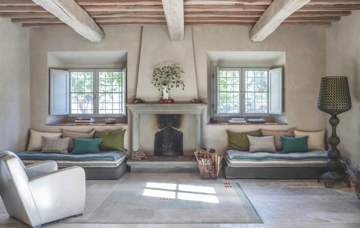 De leeshoek bij de open haard. De daybeds van gestapelde matrassen en kussens zijn op maat gemaakt. Leren fauteuil Berlino van Paola Navone voor Baxter. Schemerlamp Kabuki van Ferruccio Laviani voor Kartell.         vtwonen landelijk 7-2025 | productie Living Inside | fotografie Monica Spezia