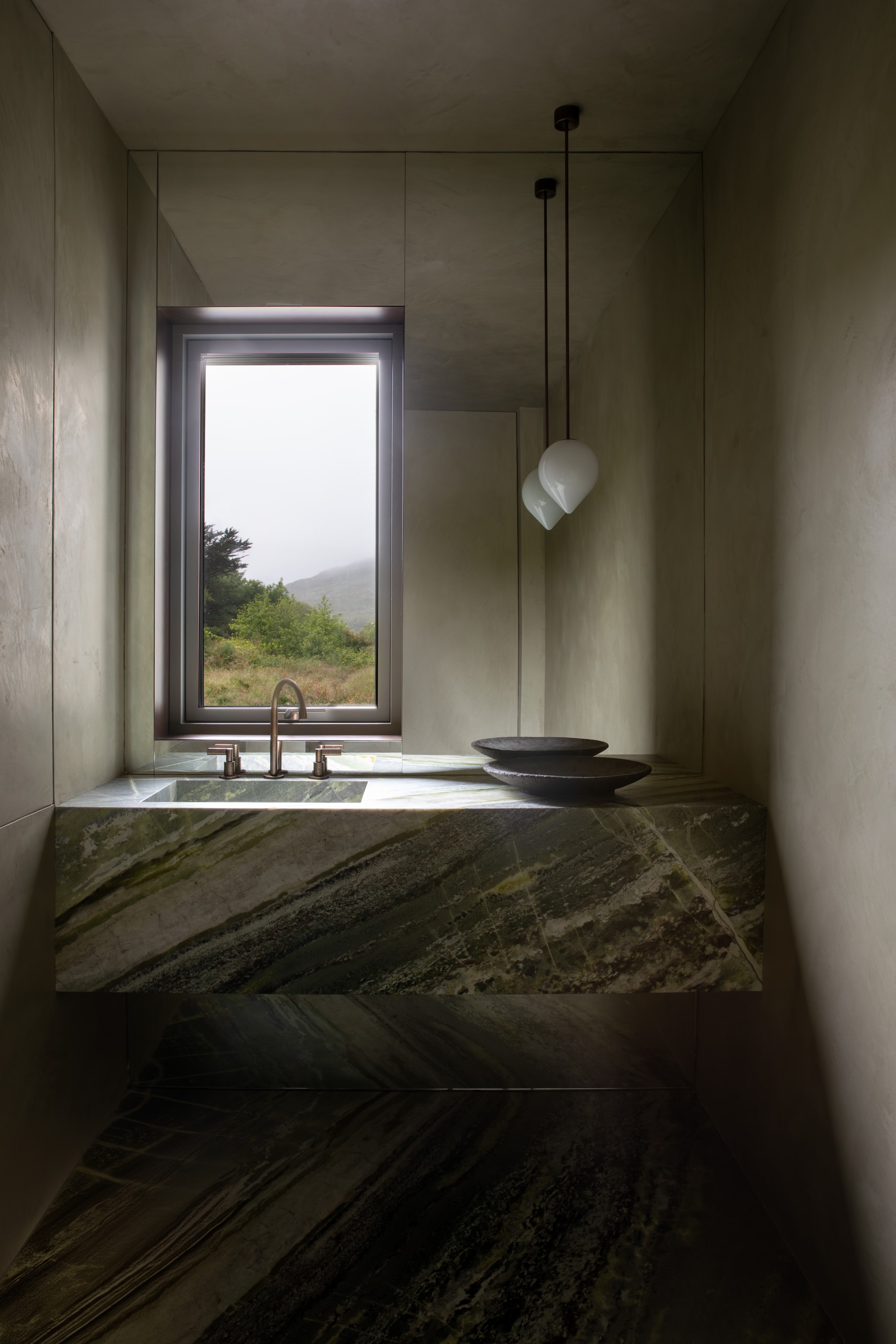Wastafel gemaakt van Irish Green-marmer, een zeldzame, lokale variant die ook wel Connemara-marmer wordt genoemd. Hanglamp van Michael Anastassiades. Stijlvol Wonen 10-2025 | Fotografie Ruth Maria Murphy