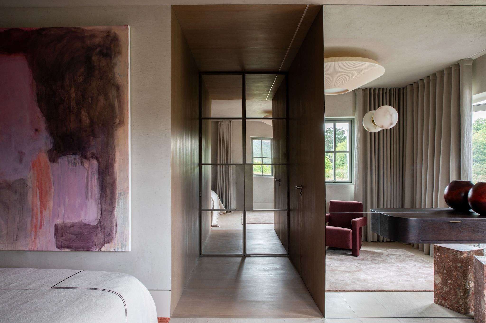 In de hoofdslaapkamer leiden deuren van gepoedercoat staal en spiegelglas naar de hal. Eikenhouten toilettafel maatwerk. Ronde lamp op spiegel Contain. Kunstwerk van de Ierse Leah Beggs. Stijlvol Wonen 10-2025 | fotografie Ruth Maria Murphy