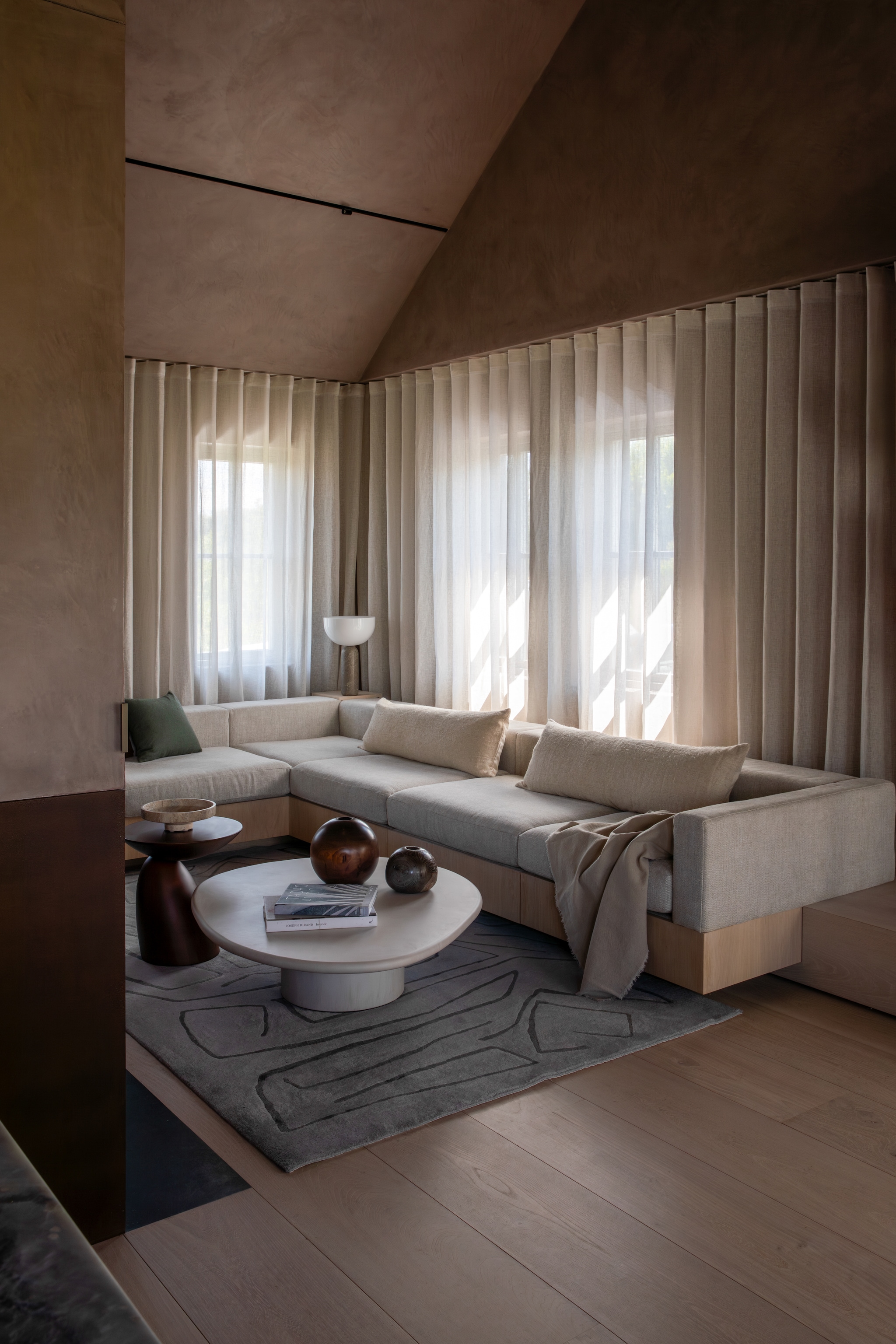 Op maat gemaakte bank, bekleed met stof van Lizzo. Bijzettafel Parabel van Eero Aarnio. Salontafel Armand & Francine. Vloerkleed ontworpen door Kelly Wearstler voor The Rug Company. Houten styling-items gemaakt door de lokale kunstenaar Richard West. Tafellamp van Lars Tornøe via New works. Stijlvol Wonen 10-2025 | Fotografie Ruth Maria Murphy