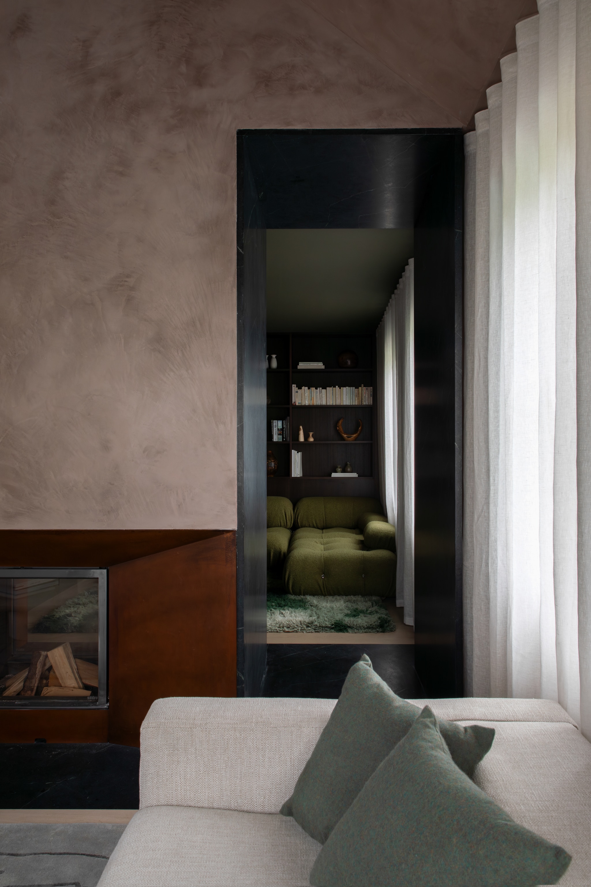 De muren zijn behandeld met gepolijst stucwerk, waar zelfgemixte pigmenten doorheen zitten. De haard is tweezijdig en heeft een basis van cortenstaal. Stijlvol Wonen 10-2025 | Fotografie Ruth Maria Murphy