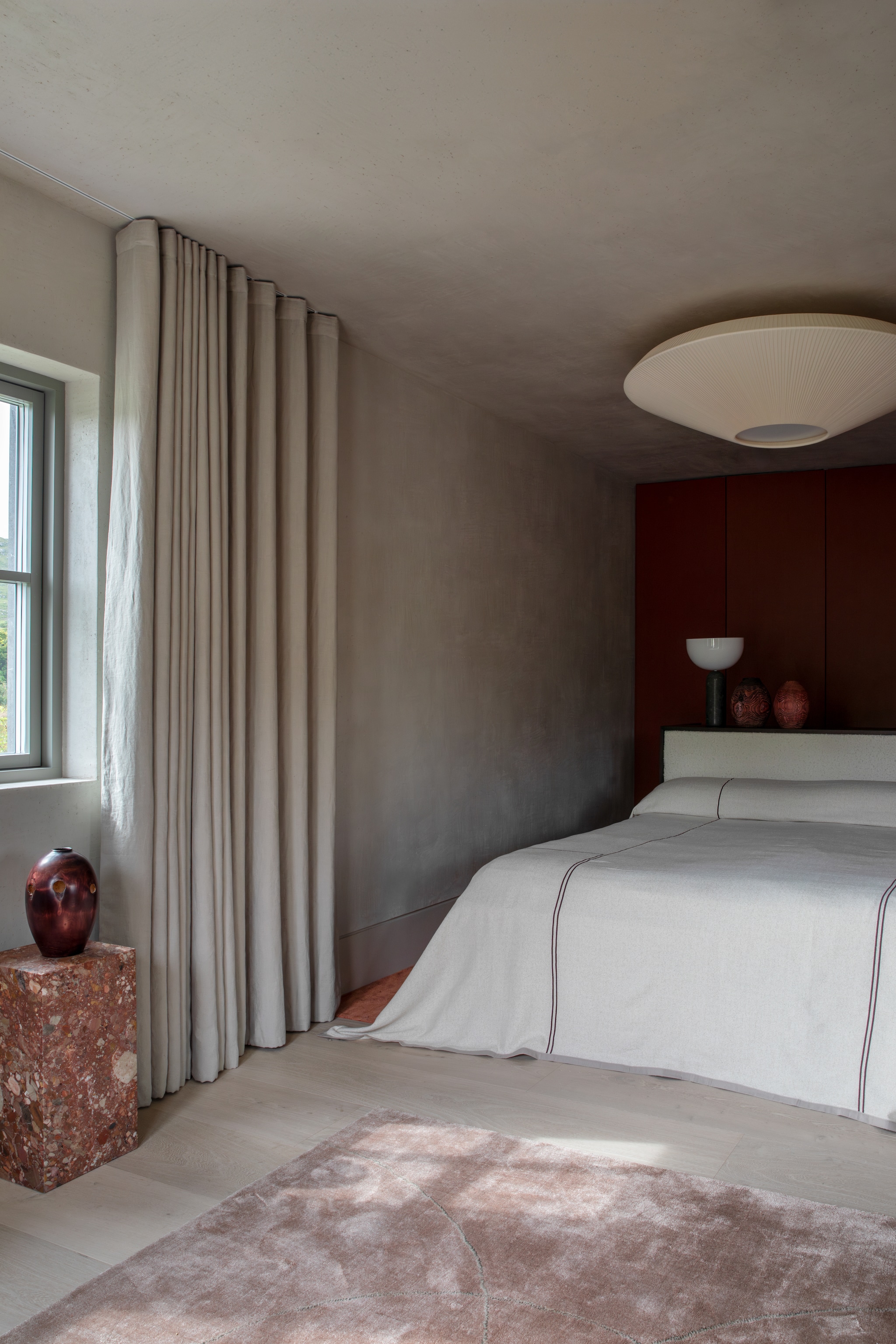 Kleed Jacaranda. Het eikenhouten hoofdbord werd donker gebeitst en bekleed met boucléstof van Dedar. Console gemaakt van Rosso Persiano-travertin. Vazen van de lokale houtdraaier Richard West. Sprei Enhance. Tafellamp met een voet van Gris du Marais-marmer van Lars Tornøe voor New works. Stijlvol Wonen 10-2025 | Fotografie Ruth Maria Murphy