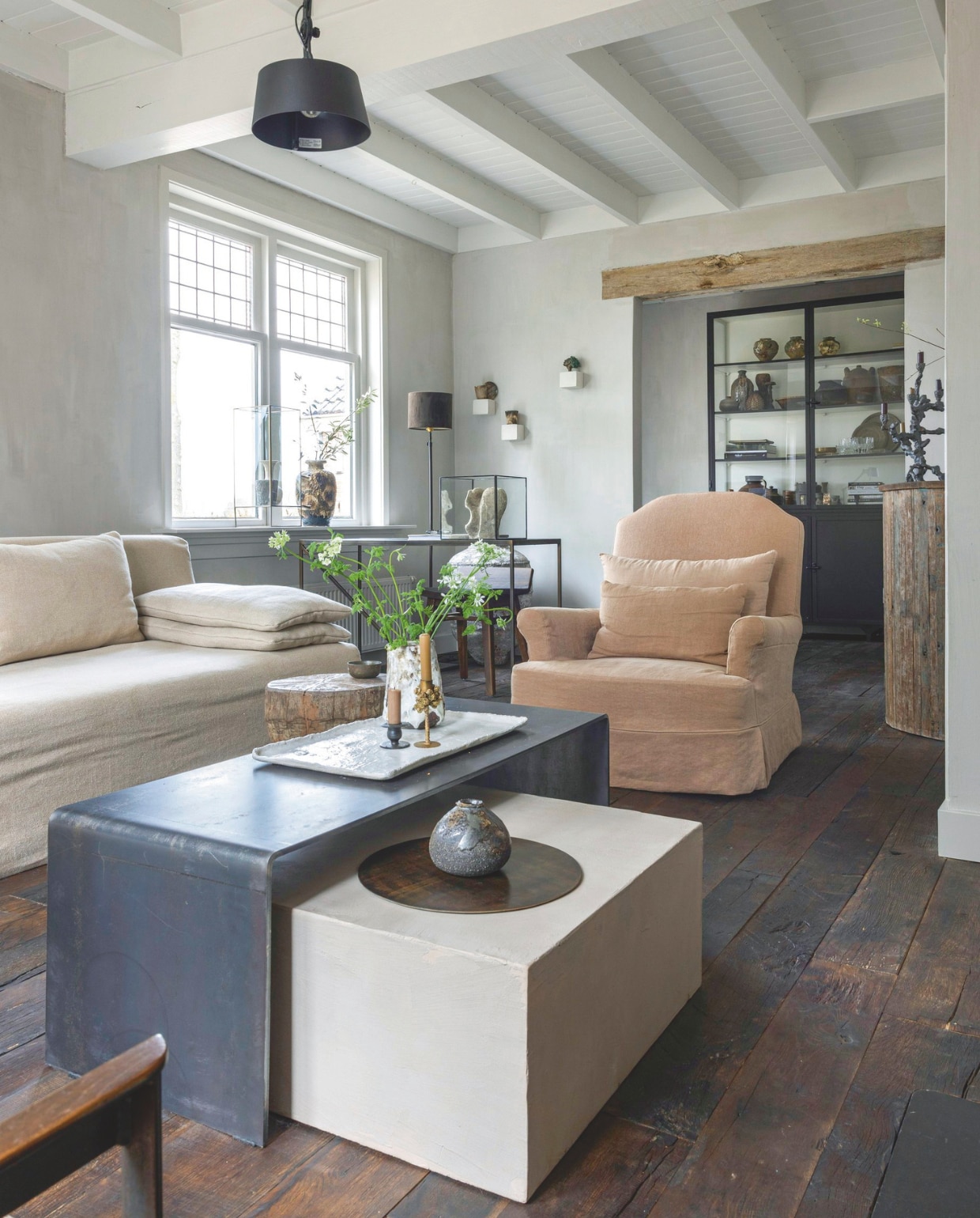 Oude eiken vloer ’t Achterhuis. Verlichting Tonone. Bank Michelle van L’Authentique. Stalen tafel Studio 085 via Atelier Natural Art. Oude fauteuil opnieuw gestoffeerd met linnen stof van Design of the Time via L’Authentique. Gestuct blok onder salontafel gemaakt met Stucco Artisan van L’Authentique. Kandelaars Zara en Weldaad. Vazen, plateau, dienblad, wandblokken en keramiek daarop Atelier Natural Art. Stalen vitrinekast Old Basics. vtwonen landelijk 08-2025 | fotografie Anneke Gambon