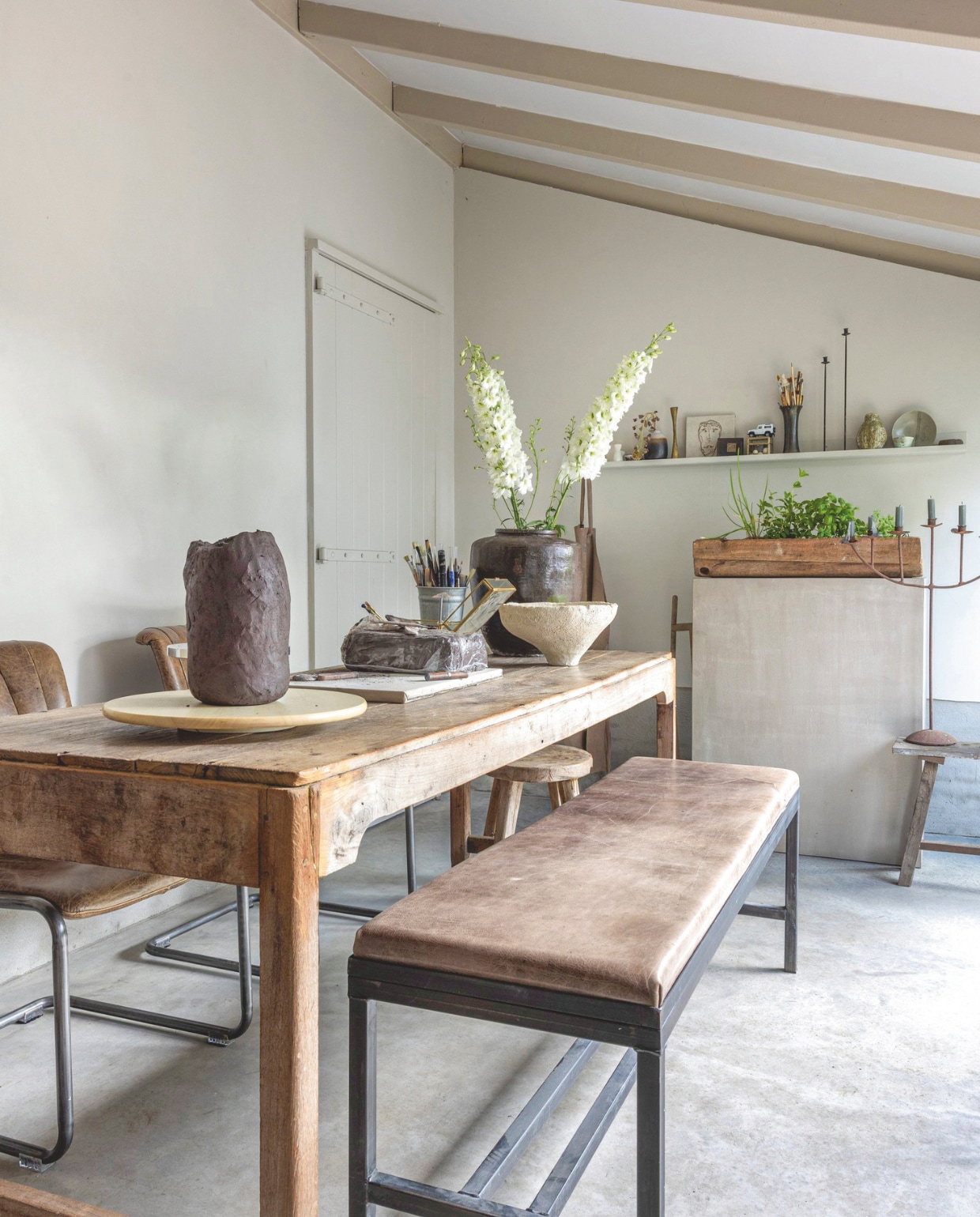 Bank, keramiek en betonnen pilaar Atelier Natural Art. Antieke tafel en houten krukken Hoffz. Vloer beton. Houten plantenbak brocantemarkt. Kandelaar antiekwinkel. vtwonen Landelijk 8-2025 | fotografie Anneke Gambon