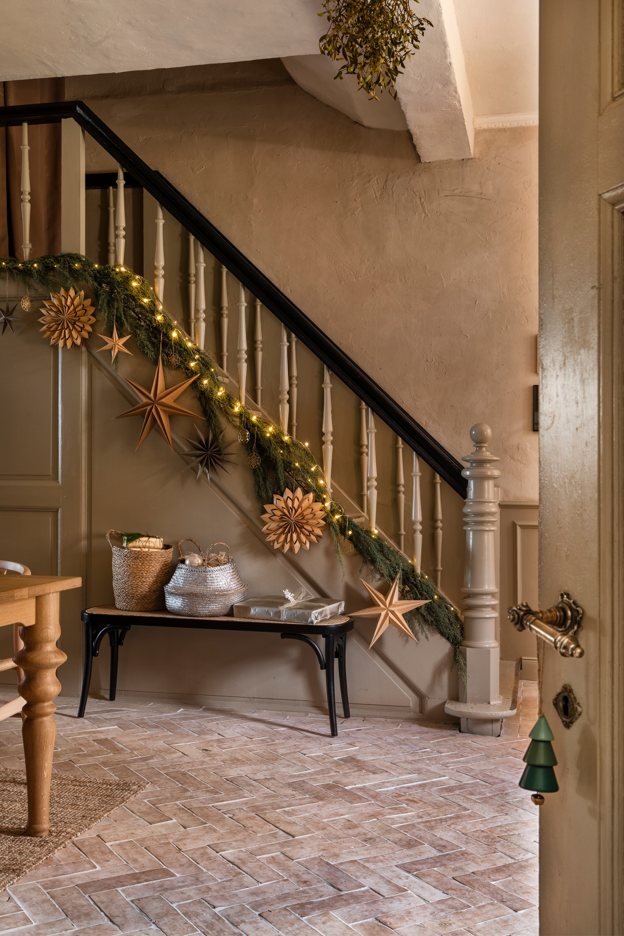 Guirlande van jeneverbes, kijk op Eefs Atelier hoe je zelf kerststerren van kraftpapieren zakken maakt of kies voor de sterren van Watt & Veke bij Nordic Nest. De leuning werd in de donkere kleur van de Thonet-bank geschilderd. vtwonen Landelijk 11-2025 | styling Miriam Hannemann | fotografie André Reuter