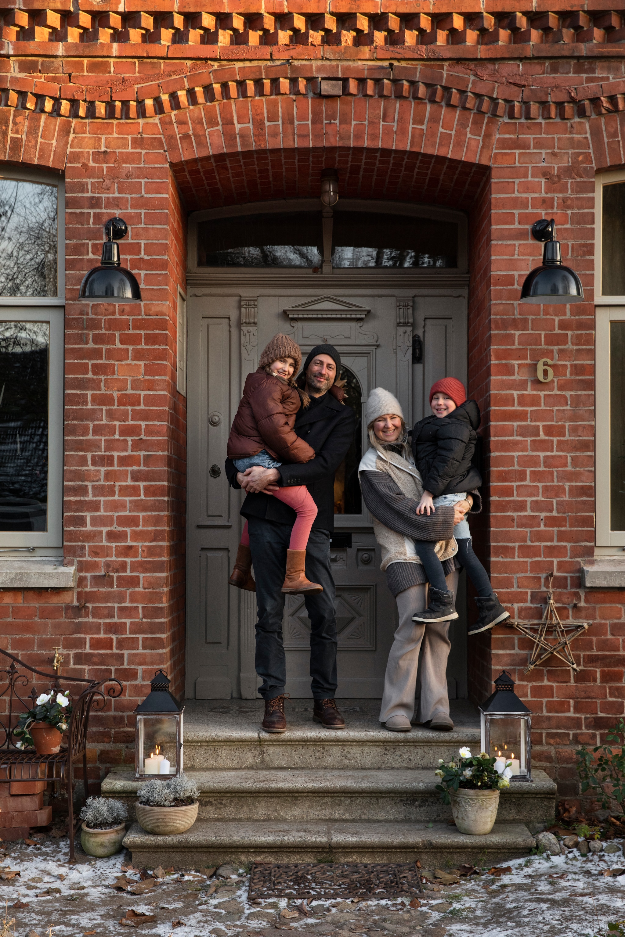 Het hele gezin bij de voordeur die wordt geflankeerd door twee oude stallampen en twee lantaarns. vtwonen Landelijk 11-2025 | styling Miriam Hannemann | fotografie André Reuter