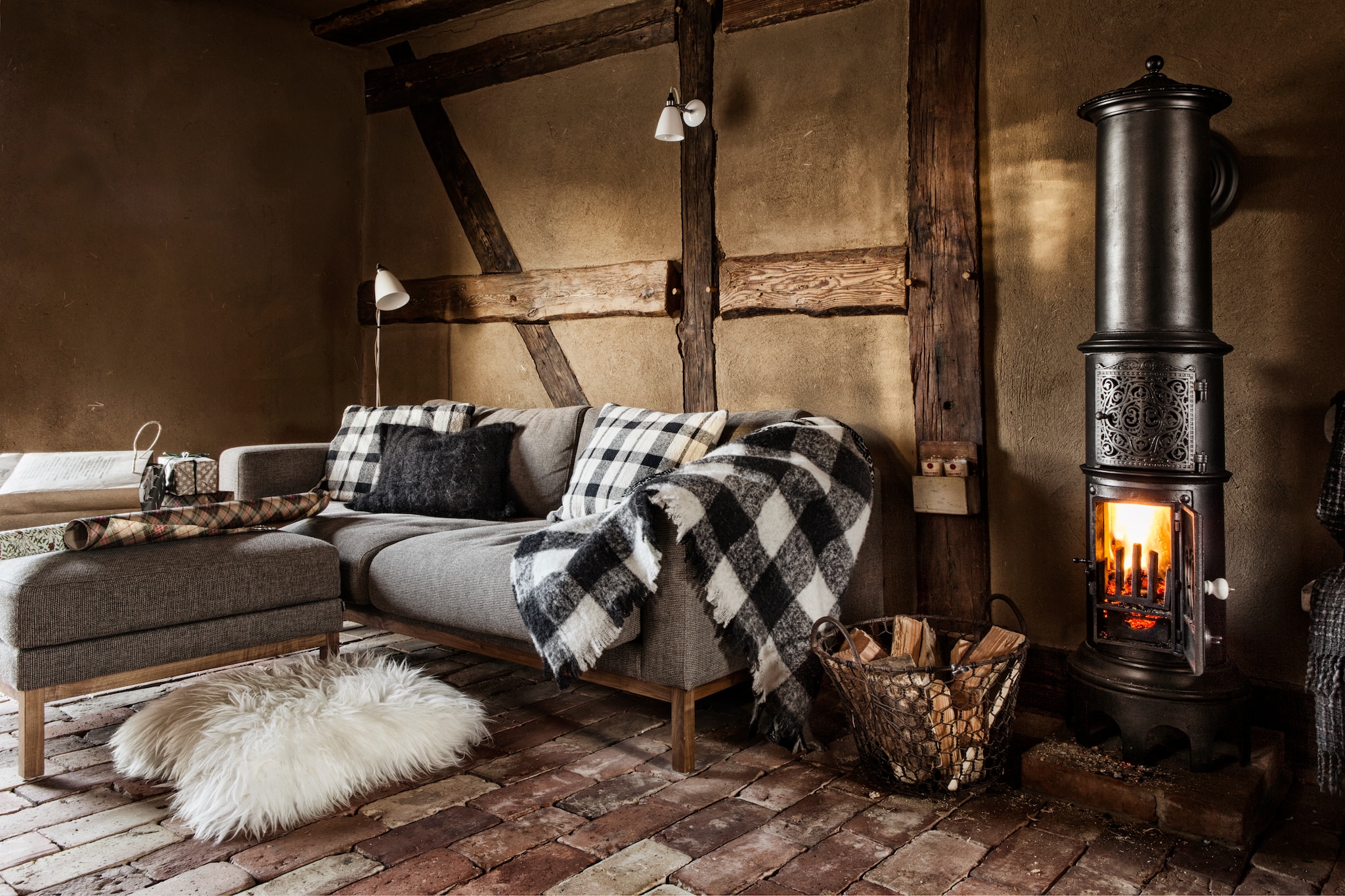 Vloer oude bakstenen. Muren leemstucwerk. Bank Bolia. Haard 19de-eeuwse Deense kolomkachel. Plaids zijn met de hand gebreid, soortgelijk bij Hoeked. Schapenvacht kussens Butlers. Gebreide zwarte kussen van een markt in Kaapstad. Lampen Hector van Original Btc. vtwonen landelijk 11-2025 | productie The Country House | styling Miriam Hannemann | fotografie André Reuter