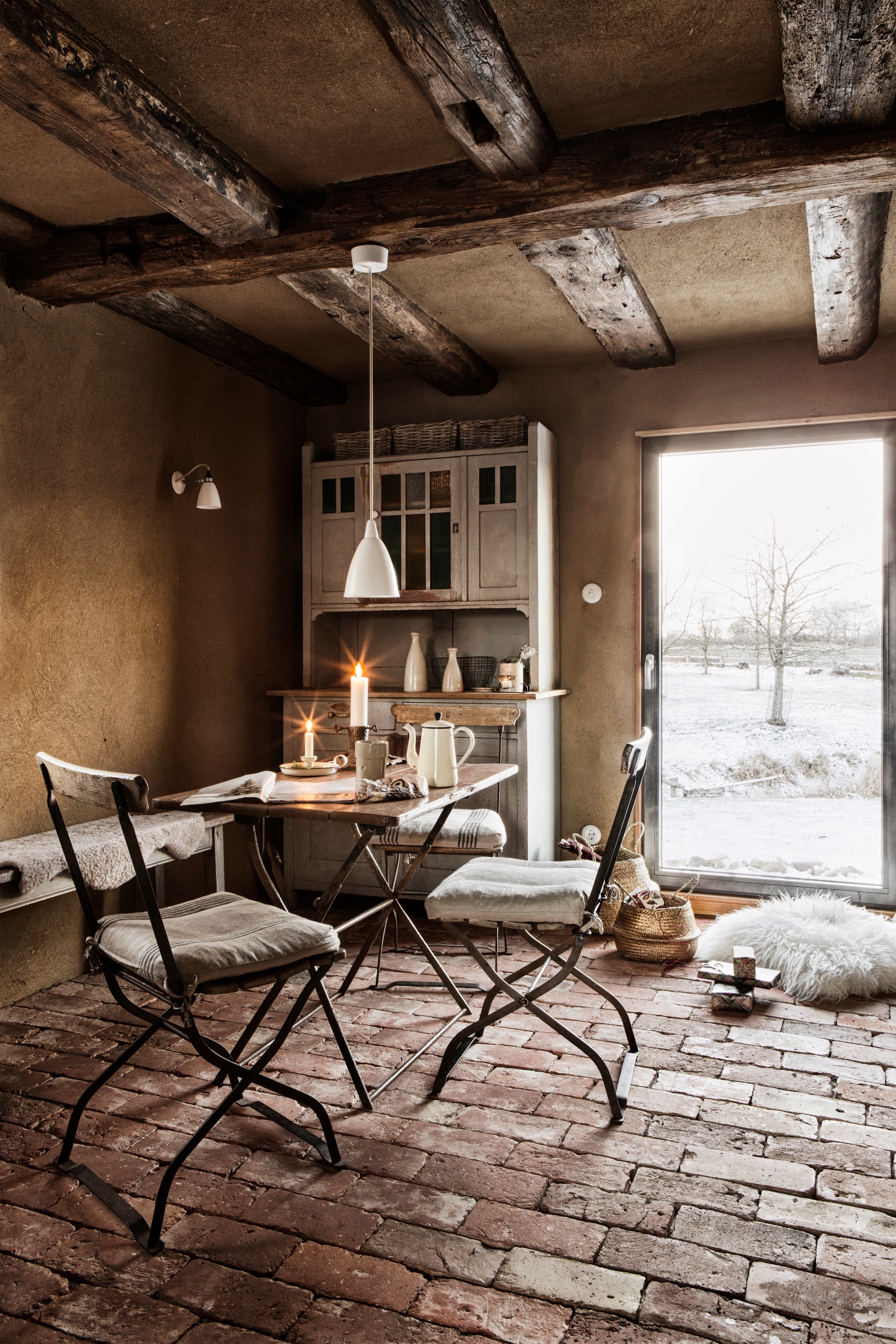 De kast, stoelen en tafel van een rommelmarkt zijn in originele staat gelaten en niet gerestaureerd. Dit deel van het huis isgebouwd van hout en aan de binnenkant bepleisterd met leem. De vloertegels komen uit een gesloopte pastorie. Manden Ikea. Schapenvacht kussens Inno Living. Soortgelijke hanglamp Louis Poulsen. Handgemaakte aardewerk flessen, bekers en vazen ​​Töpferei Distelkamp. vtwonen landelijk 11-2025 | productie The Country House | styling Miriam Hannemann | fotografie André Reuter