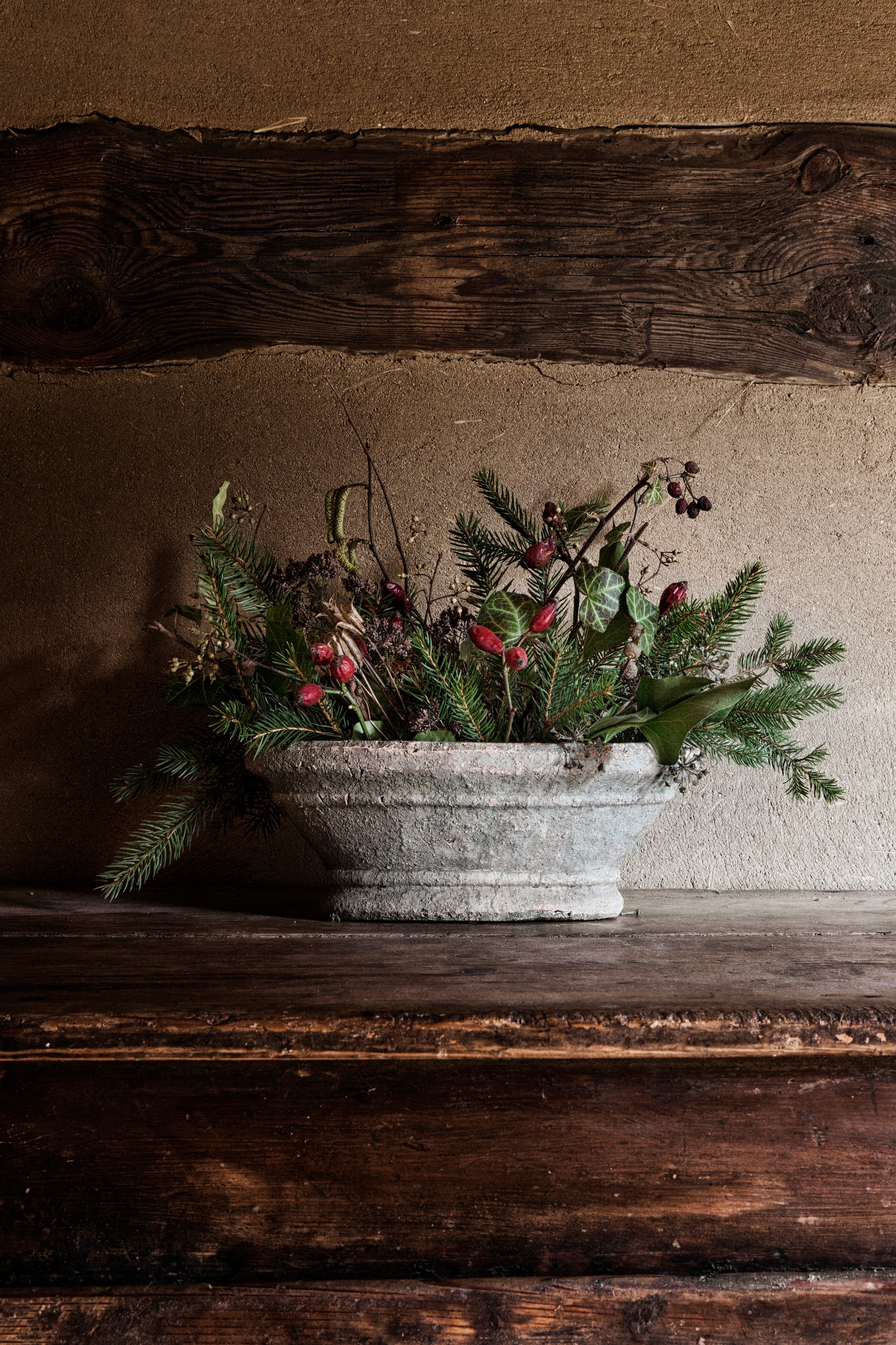 Subtiele kerstversiering van dennentakken, rozenbottels en klimop in een vintage schaal. Broodkast vintage. vtwonen landelijk 11-2025 | productie The Country House | styling Miriam Hannemann | fotografie André Reuter