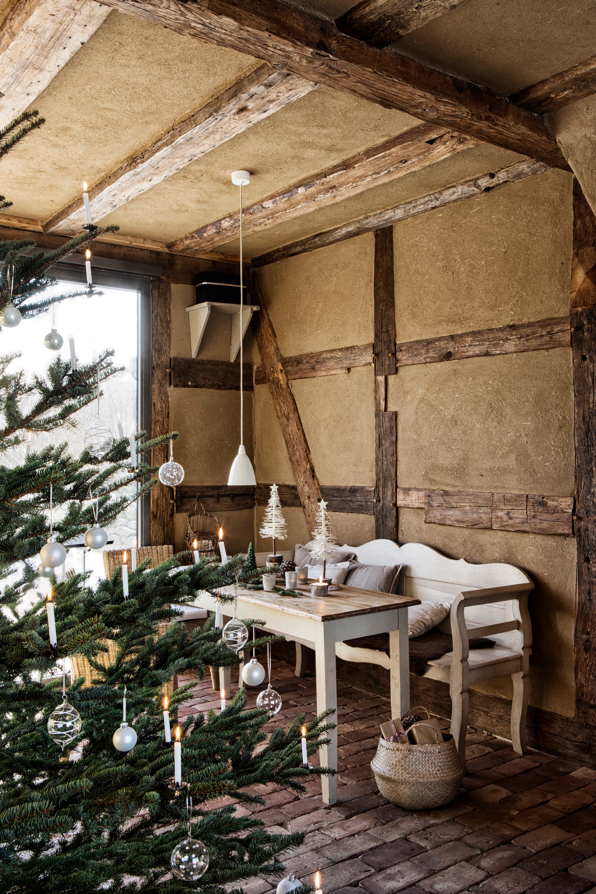 De kerstboom kapt de familie zelf bij een boswachter in het dorp verderop. De versiering houden ze ingetogen met echte kaarsjes. Kerstboomkaarsjes vind je bij Het Bijenhuis. Mand Ikea. Soortgelijk:  hanglamp Louis Poulsen, tafel en bank Van Dijk & Ko. vtwonen landelijk 11-2025 | productie The Country House | styling Miriam Hannemann | fotografie André Reuter