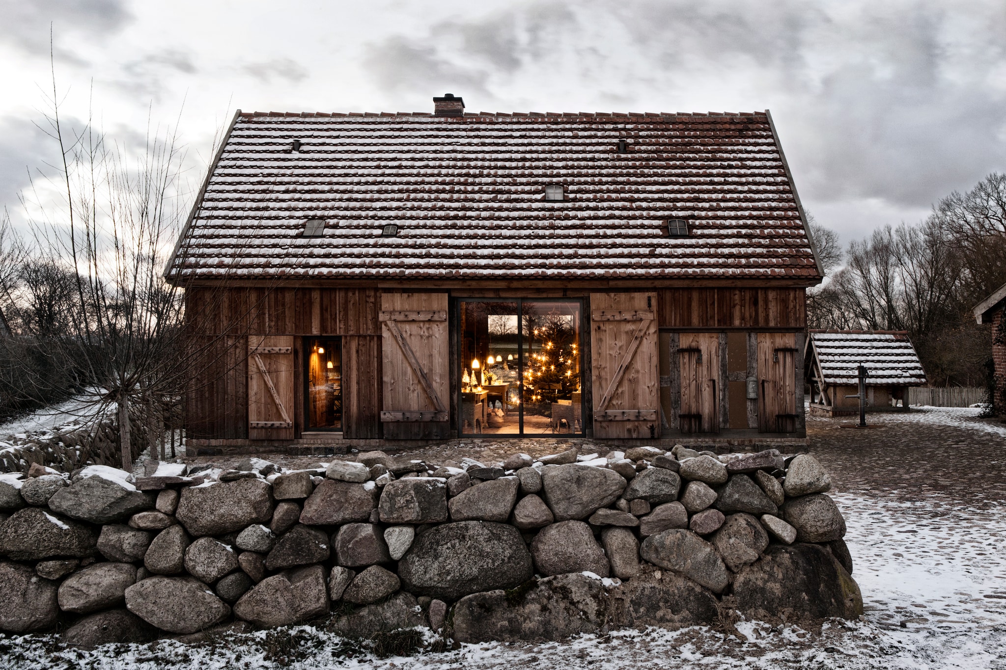 Het terras is geplaveid met veldstenen, verzameld uit de omliggende velden. Het dak is bedekt met historische, handbeschilderde dakpannen. De ene helft van het huis is gebouwd in de traditionele vakwerkstijl en bepleisterd met leem. De andere bestaat volledig uit hout. vtwonen landelijk 11-2025 | productie The Country House | styling Miriam Hannemann | fotografie André Reuter