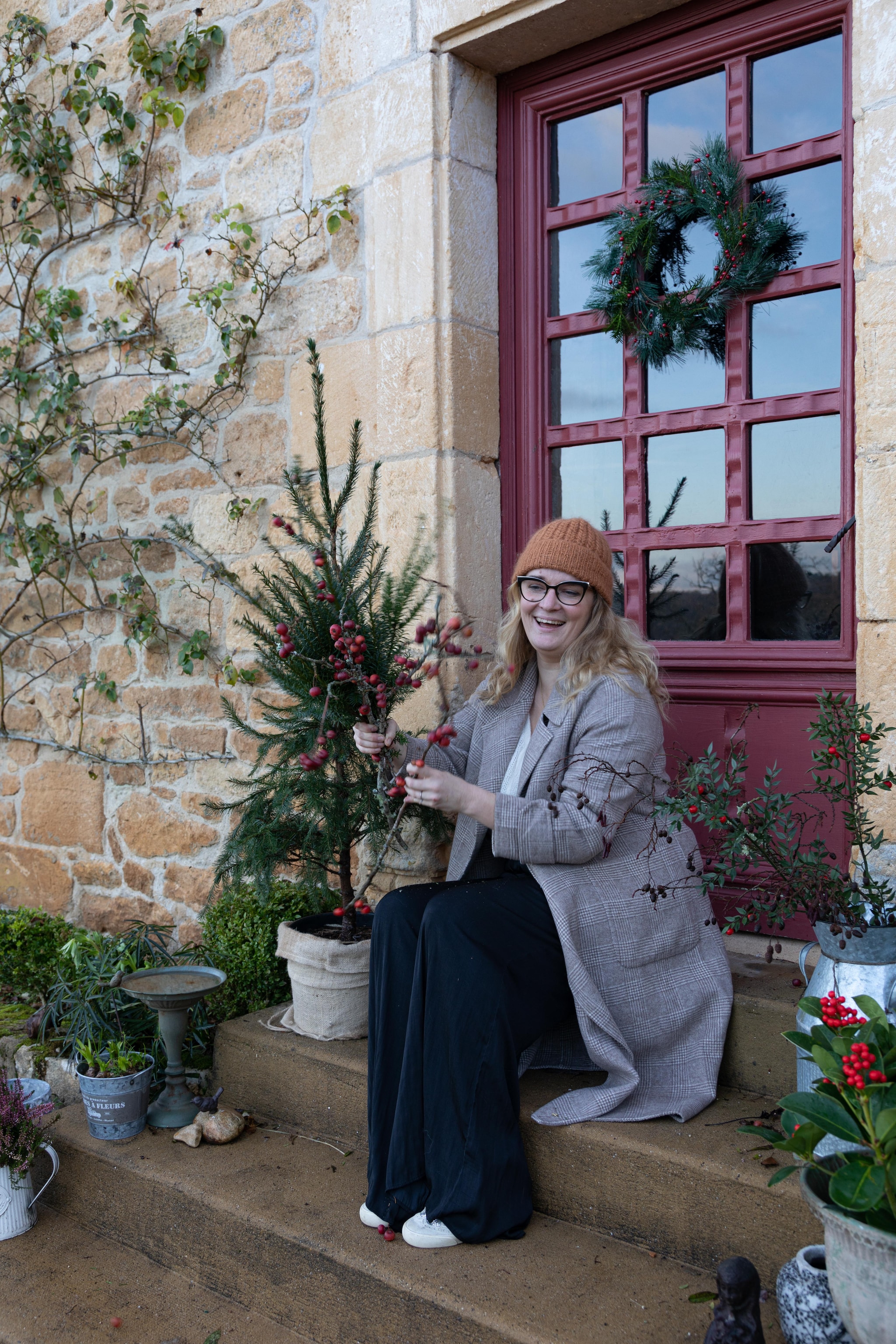 Chloé op de trap naar de voordeur van haar boerderij. De orginele, verouderde deur van het huis is vervangen door een nieuwe die goed past bij de uitstraling van de boerderij. Het metselwerk buiten is hetzelfde als binnen. De muren zijn gekalkt in traditioneel oker. vtwonen Landelijk 11-2025 | styling Wilma Custers | fotografie Fabienne Delafraye