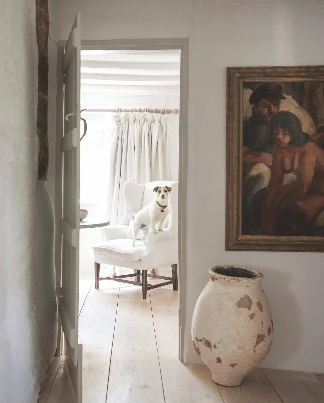 Plafond en muur verfkleur Yes Your Honour van Fired Earth. Kunstwerk van onbekende kunstenaar. Witte kruik uit Mallorca. Fauteuil Anton & K. Gordijnen Tinsmiths. vtwonen landelijk 8-2025 | productie Living Inside | styling Ali Heath | fotografie Emma Lewis