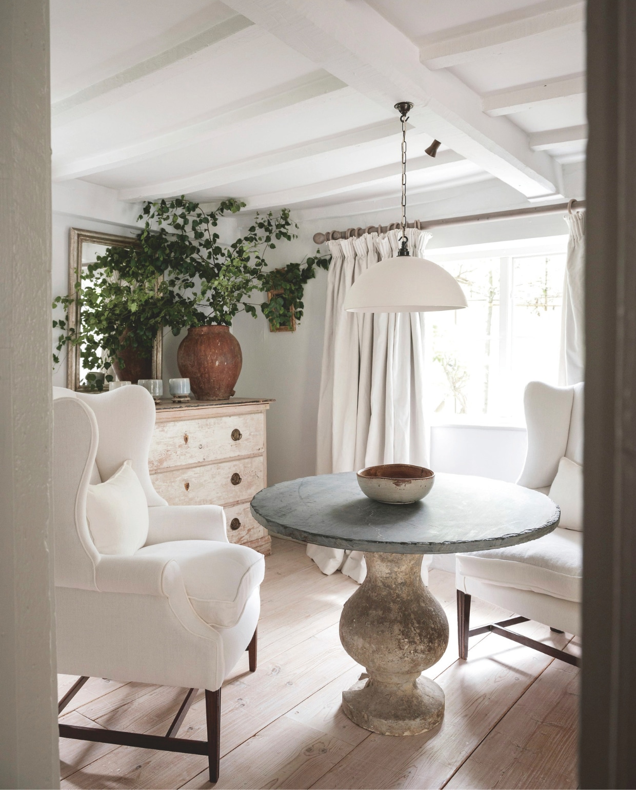 Plafond en muur verfkleur Yes Your Honour van Fired Earth. Fauteuils, hanglamp, ladekast en kandelaars Anton & K. Tafel uit de Provence. Vaas op ladekast, spiegel en Zweedse 17de-eeuwse kom op tafel antiek. Gordijnen Tinsmiths. vtwonen landelijk 8-2025 | productie Living Inside | styling Ali Heath | fotografie Emma Lewis