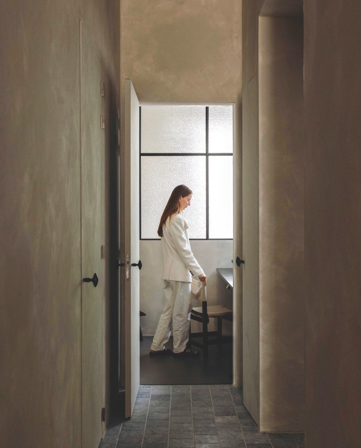 Deuren en muren geverfd met betonverf in Silk van Beton Cire Webshop. Belgisch hardstenen tegels antiek. Wand van glas en staal Gillissen Ontwerp. Stoel Marktplaats. vtwonen landelijk 8-2025 | fotografie Stie De Neve