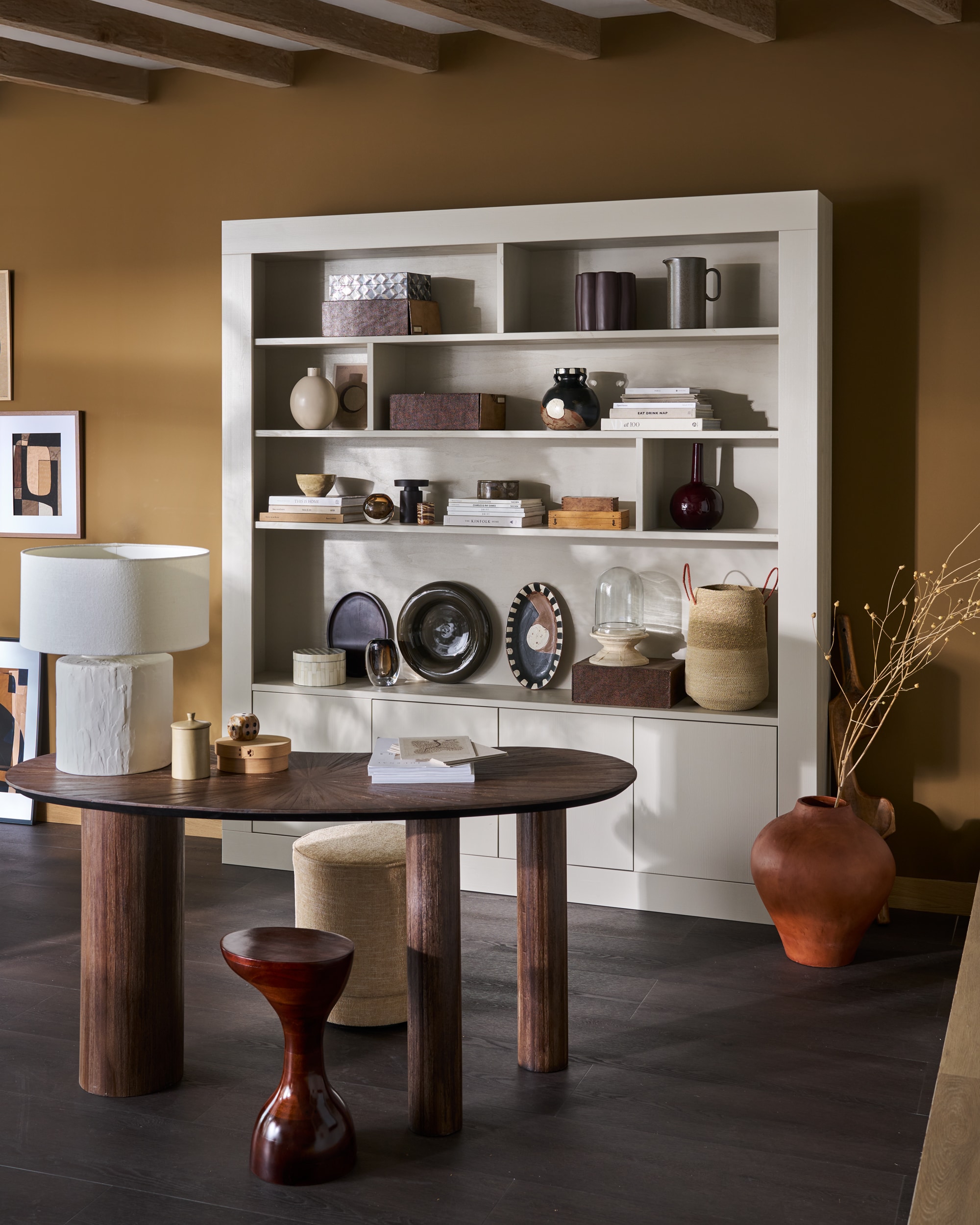 vtwonen wandkast Wallcover, grenen, dust, 210x31x229 cm (bxdxh) € 1499,-, vtwonen poef Pearl, melange stof, naturel, 40x45 cm (Øxh) € 199,-.M.m.v. woood.nl (bureau), urbannatureculture.com (tafellamp, bijzettafel, oranje pot, geschulpte paarse bloempot, donkergroene schaal), vansand.nl (Little Greene muurverf Light Bronze Green no. 123), zarahome.com (ovalen schalen, beschilderde vaas), burbriantiek.nl (archiefdozen), weldaad.com (stolp op voet, mand). Aubergine kandelaar van vtwonen (shop.vtwonen.nl). Overig privébezit. vtwonen 11-2025 | styling Cleo Scheulderman | fotografie Jeroen Van der Spek