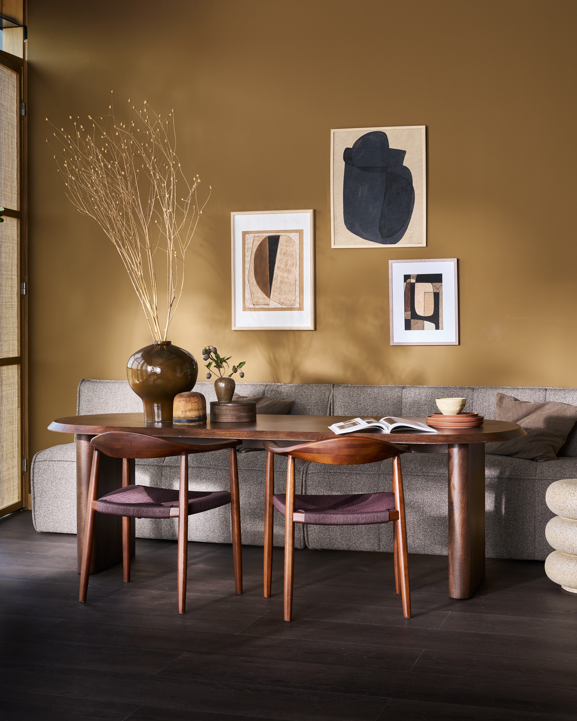 vtwonen eetbank Cluster, bouclé, 4 kleuren, 163x76x88 cm (bxdxh) € 799,-, vtwonen eettafel Ellips, mangohout, walnoot, 240x90x75 cm (lxbxh) € 1599,- of 180x90x75 cm (lxbxh) € 1299,-, vtwonen eetkamerstoel Embrace, beukenhout, donkerbruin, 64x53x76 cm (bxdxh), set van 2 € 558,-.M.m.v. urbannatureculture.com (grote vaas), hm.com (grafisch kussen), woood.nl bijzettafel), ilsevanstoltz.com (art prints), vansand.nl (Little Greene muurverf Light Bronze Green no. 123), zarahome.com (ronde doos). Overig privébezit. vtwonen 11-2025 | styling Cleo Scheulderman | fotografie Jeroen Van der Spek