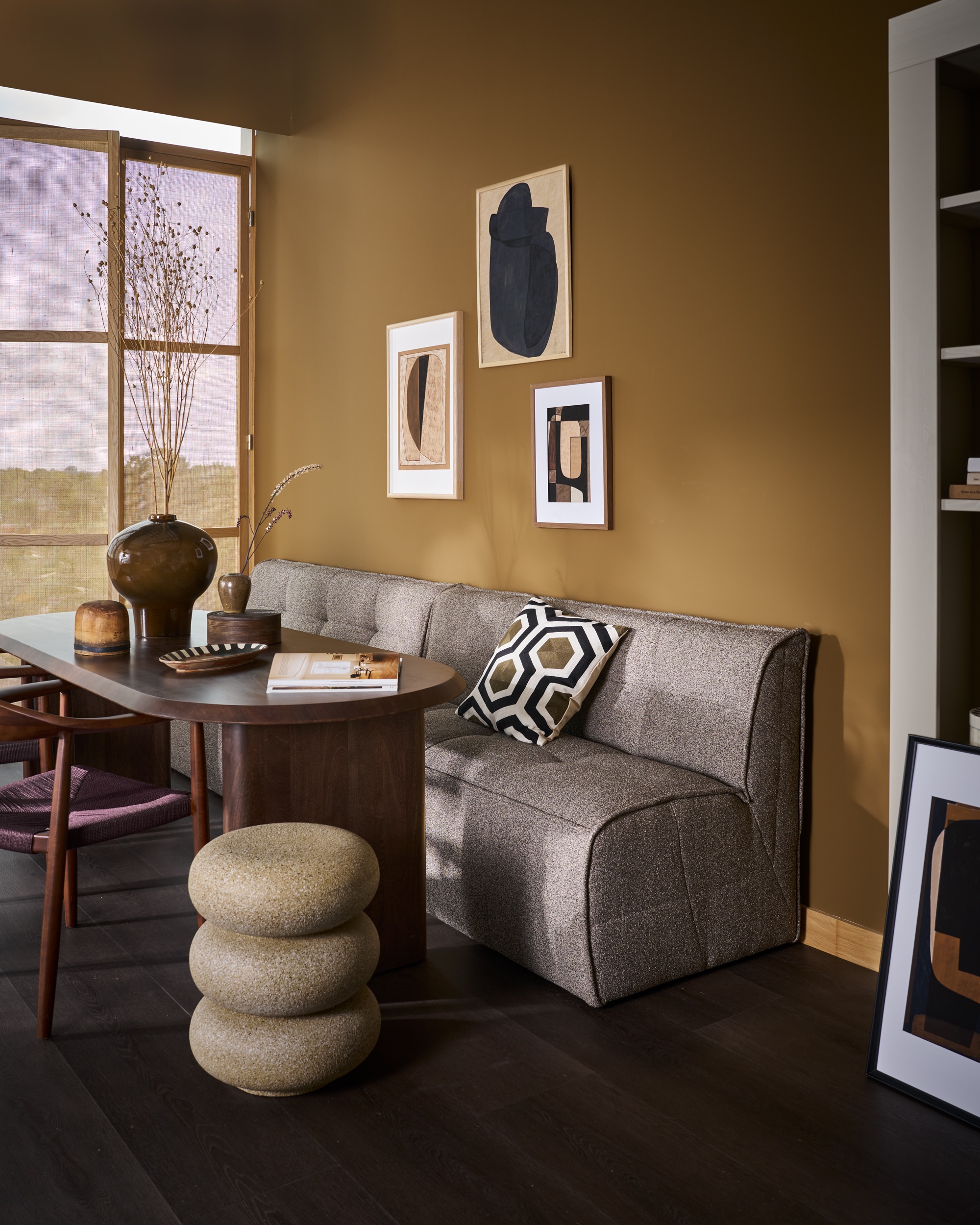 vtwonen eetbank Cluster, bouclé, 4 kleuren, 163x76x88 cm (bxdxh) € 799,-, vtwonen eettafel Ellips, mangohout, walnoot, 240x90x75 cm (lxbxh) € 1599,- of 180x90x75 cm (lxbxh) € 1299,-, vtwonen eetkamerstoel Embrace, beukenhout, donkerbruin, 64x53x76 cm (bxdxh), set van 2 € 558,-.M.m.v. urbannatureculture.com (grote vaas), hm.com (grafisch kussen), woood.nl bijzettafel), ilsevanstoltz.com (art prints), vansand.nl (Little Greene muurverf Light Bronze Green no. 123), zarahome.com (ronde doos). Overig privébezit. vtwonen 11-2025 | styling Cleo Scheulderman | fotografie Jeroen Van der Spek