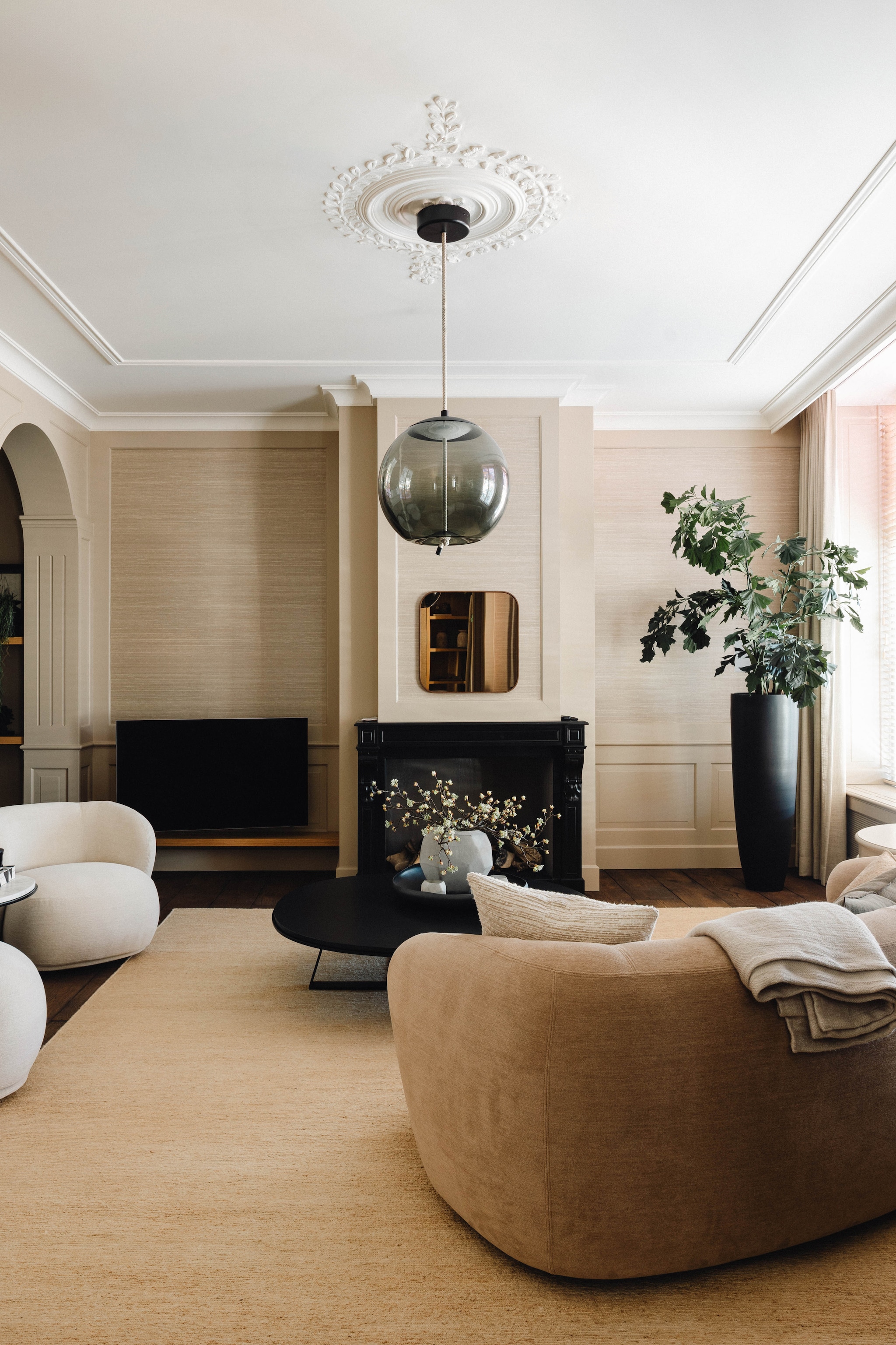 De originele elementen zijn bewaard gebleven, zoals de rondboog en het pleisterwerk op het plafond. Bank en fauteuil René en salontafel Judd van Meridiani. Kleed Amar van Carpetlinq. Hanglamp Knot van Brokis. Spiegel Camber van Ethnicraft. Stijlvol Wonen 9-2025 | fotografie Stie de Neve