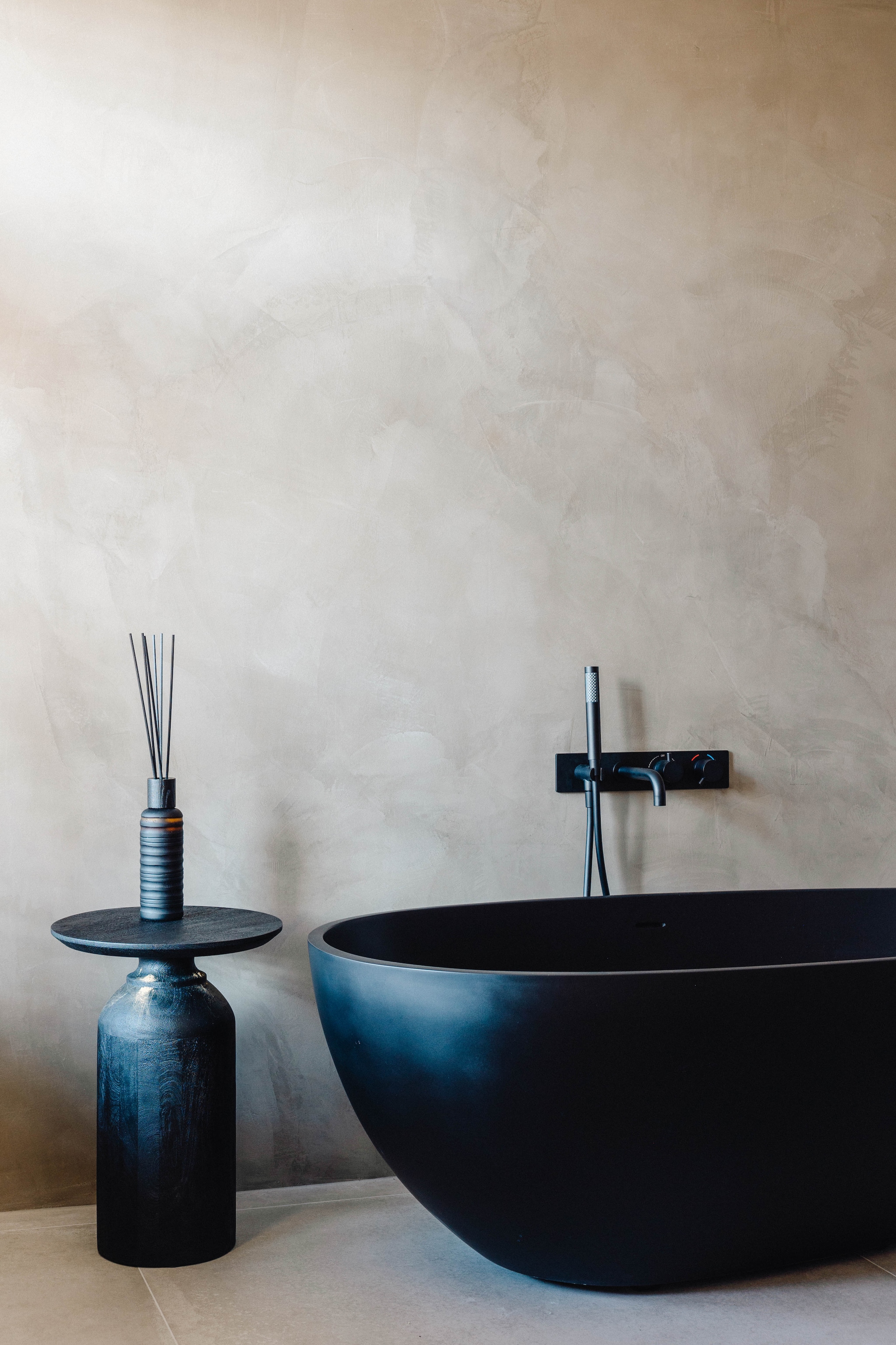 Ingetogen kleuren zorgen voor rust in de badkamer. Het bad steekt mooi af bij de achterwand van beton ciré. Stijlvol Wonen 9-2025 | fotografie Stie de Neve