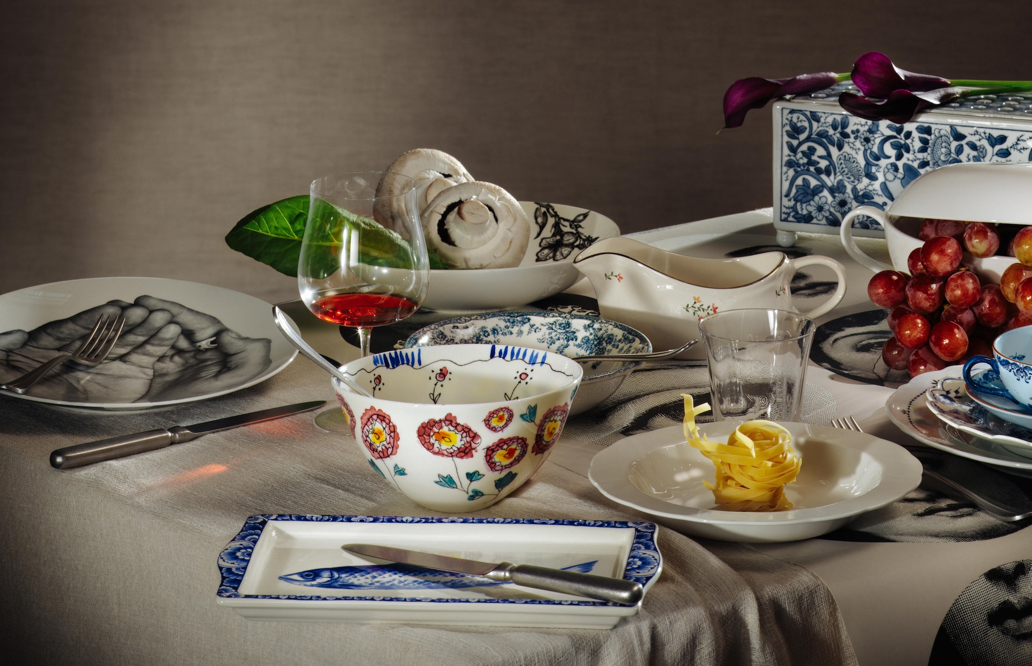 Bernardaud bord Les Mains € 165,- (mekshop.nl). Serax bestek, set van 24 € 444,-, serveerschaal, door Tomorrowland, porselein, zwarte bloemenprint € 18,-, kom Anemone, door Marni € 82,-, pastabord € 17,-, wijnglas € 16,-, waterglas € 12,-, allemaal uit de collectie Silhouette door Sergio Herman (serax.com). Zara Home schaal bloemenprint, porselein, blauw en wit € 8,-, juskom, porselein, bloemenprint € 20,-, soepterrine, porselein, wit € 70,- (zarahome.com). Heinen Delftsblauw schaal Haring, keramiek, wit met blauw € 23,- (supermatique.com). &Klevering vaas, porselein, blauw € 70,- (klevering.com). Ikea bord Upplaga, wit, 28 cm (Ø) € 5,- (ikea.com). Gastronomie Nostalgie bord Zwiebelmuster, porselein, blauw € 30,-, Rörstrand soepkom met schotel, porselein, blauw en wit € 40,- (gastronomie.nostalgie). Kniphal tafelkleed, beige (kniphal.nl). Cole & Son behang, door Fornasetti (cole-and-son.com). Stijlvol Wonen 10-2025 | Styling Djamilla van Brussel | Fotografie Benning & Gladkova