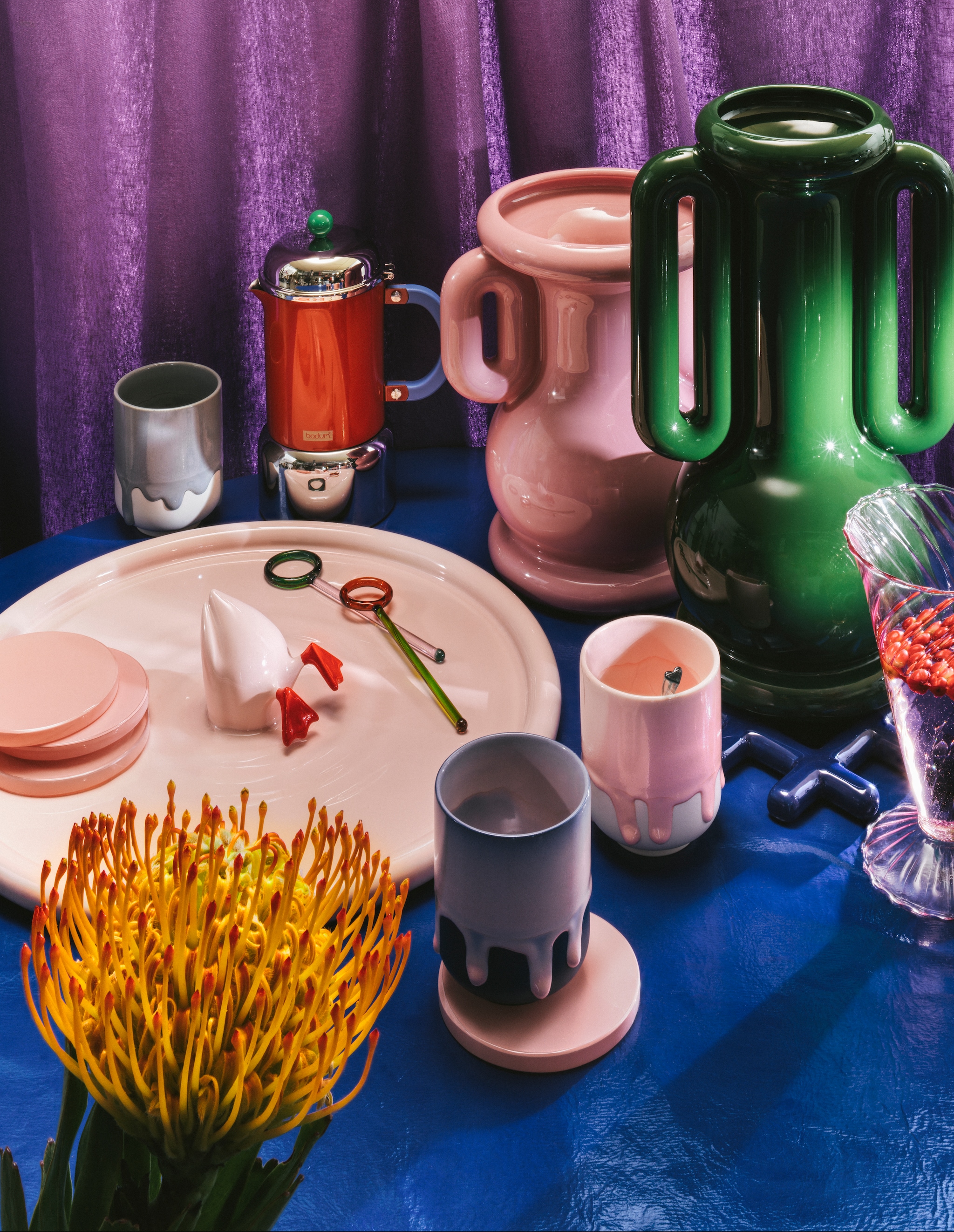 &Klevering vazen Amfora, handgemaakt keramiek, groen, 36 cm (h) € 150,- en roze, 26,5 cm (h) € 125,-, onderzetter Trivet Grid, aardewerk, donkerblauw € 30,- (klevering.com). Bodum koffiepercolator Chambord, rood, rvs € 98,- (debijenkorf.nl). Arhoj kopjes Slurp, geglazuurd porselein € 30,- (arhoj.com). Polspotten bord Diving Duck, geglazuurd aardewerk, lichtroze € 130,- (polspotten.nl).Urban Nature Culture onderzetters, glas, roze, set van 4 € 23,-, cocktail roerstaafjes, borosilicate glas, set van 2 € 18,- (urbannatureculture.com). Søstrene Grene glas € 9,-, lepel in mok € 2,- (sostrenegrene.com). Kniphal stof, blauw (kniphal.nl). Folk and Fiber doek, Italiaanse linnen, purple sky € 20,- (folkandfiber.nl). Stijlvol wonen 10-2025 | Styling Djamilla van Brussel | fotografie Benning & Gladkova