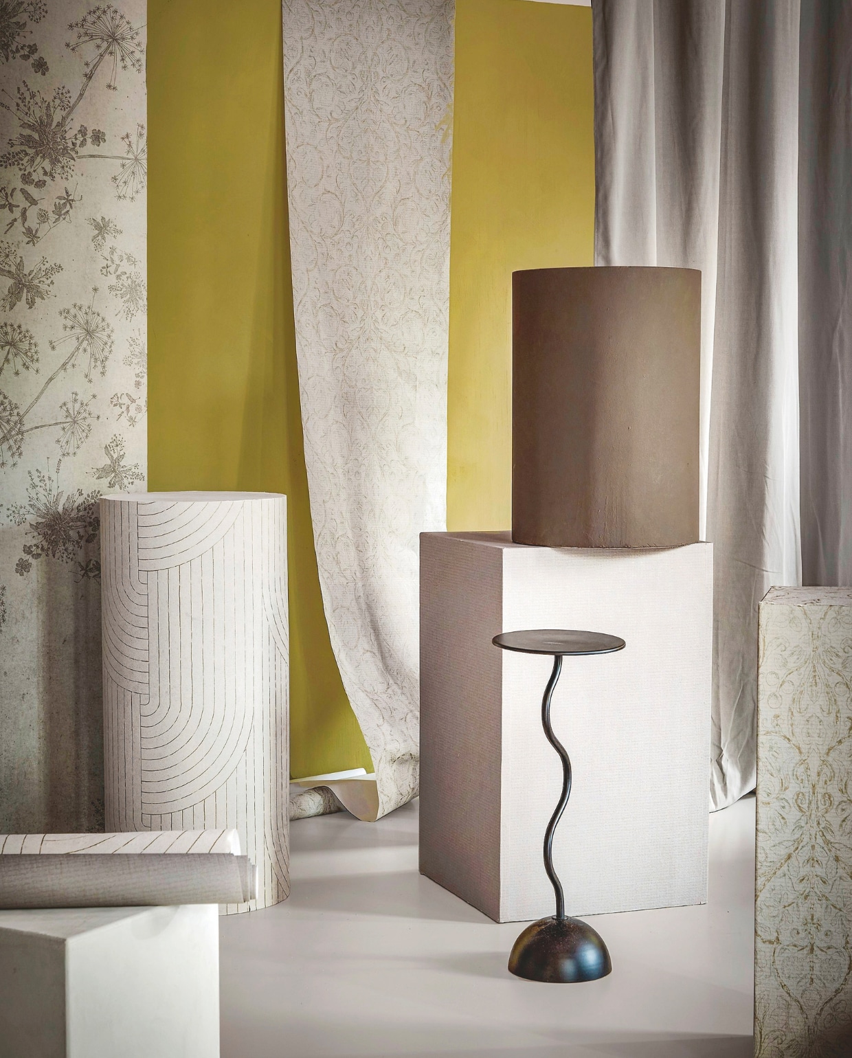 vtwonen fotobehang Wild Flower, per m² € 17,74 (strook links). vtwonen behang Classic Curl, light grey, 53 cm x 10 m (bxl), per rol € 33,99 (strook rechts en blok rechts). vtwonen behang Broom Bow, flax, 53 cm x 10 m (bxl), per rol € 33,99 (ronde pilaar). vtwonen behang Linnen, mirre, 53 cm x 10 m (bxl), per rol € 33,99 (middelste blok). vtwonen muurverf krijtmat, forest (wand), warm brown (bruin blok), linnen (blok linksonder), 1 liter € 27,99. vtwonen kant-en-klaargordijn Denim, flax, lichtdoorlatend met ring, 140x270 cm (bxh) € 63,99. vtwonen 9-2025 | styling Sanne Ketelaar | fotografie Peggy Janssen