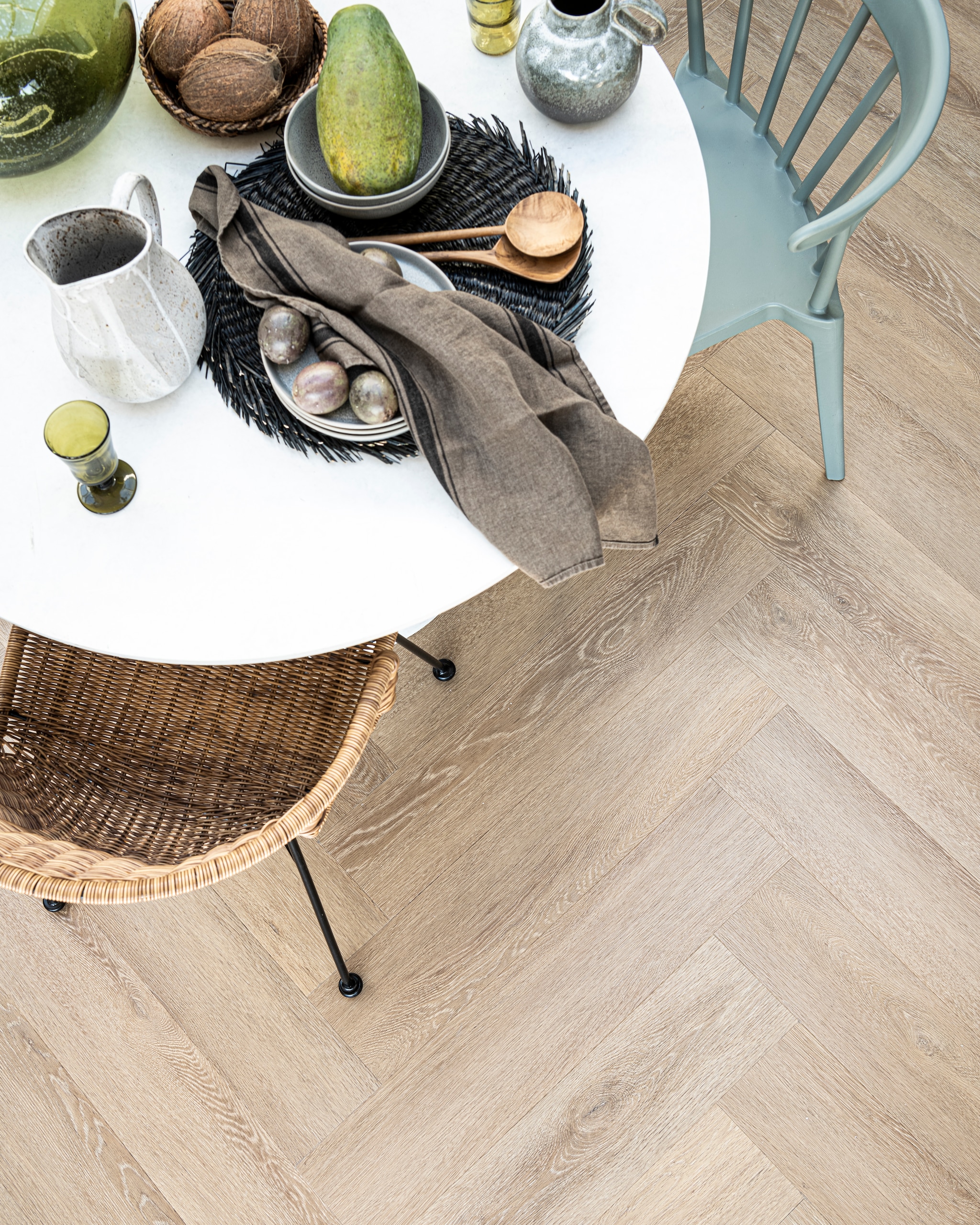 PVC Vloer Herringbone Sun Kissed, 76,5×15,3 cm, verkrijgbaar in dryback en click 75×15 cm. M.m.v. basiclabel.nl (eettafel en eetkamerstoelen van Woood), vtwonen.nl (grijze borden, kommen, placemats, kruik met handvat, alles van Bloomingville), sissy-boy.com (grijze kan wit geverfd), hm.com (mand), paviljoennoord.com (groen wijnglas, groene waterglazen, houten bestek, groene glazen vaas, theedoek). Overig privébezit. vtwonen 06-2021 | productie Tanja Saarberg | styling Danielle Verheul | fotografie Sjoerd Eickmans