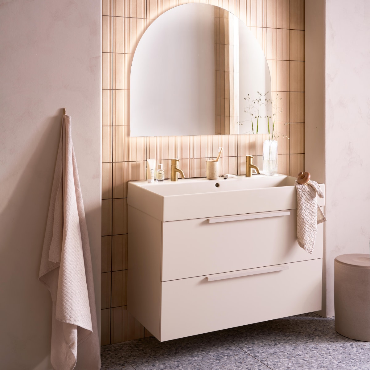 Op de wand tegels Earth Calce 3D Decor, 20x20 cm, per m² € 64,50. Op de vloer tegels Terrazzo Smoke Flakes, 60x120 cm, per m² € 74,50. Spiegel Design, half rond met indirecte verlichting, 100x80 cm € 998,-, ook verkrijgbaar zonder verlichting en in andere afmetingen. Kunststof onderkast Tidy in matzand, twee lades met handgreep, 120x40,5x40 cm (bxdxh) € 1362,-, Top Solid wastafel Wide in zand, twee kraangaten, 120x41x20 cm (bxdxh) € 1095,-. M.m.v. plieger.nl (kranen Roma in geborsteld goud), vtwonen.nl/shop (kruk van Serax), zarahome.com (badlaken, beker, zeep, kimono), lelabofragrances.com (parfum). Overig privébezit. vtwonen 09-2024 | fotografie Jeroen van der Spek | styling Cleo Scheulderman